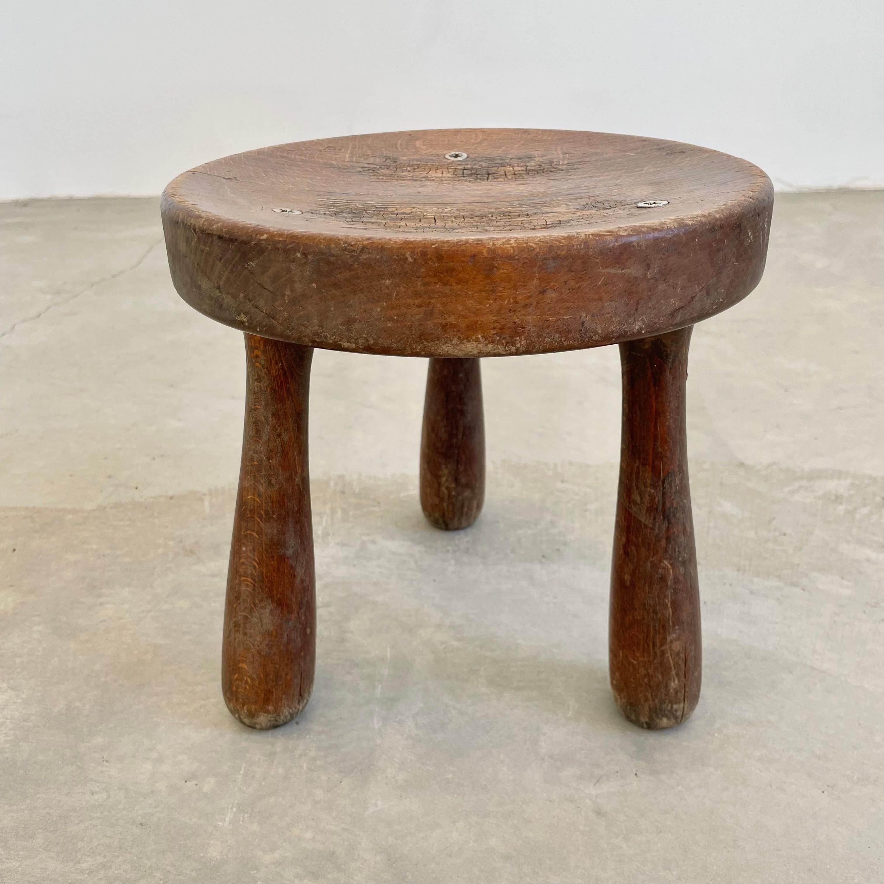 Beautiful wooden tripod stool made in France, circa 1950s. Substantial and chunky seat with sturdy club legs that taper out at the bottom. This stool has a thick round seat with 3 nickel screws. Great patina and grain to the wood. Functional stool.