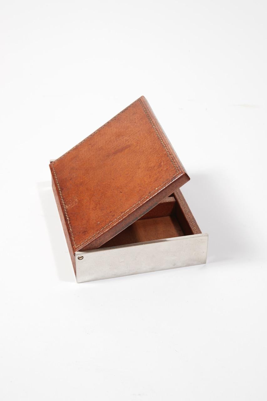 A chromed metal and saddle-stitched brown leather cigar box. Two interior compartments. Stamped 