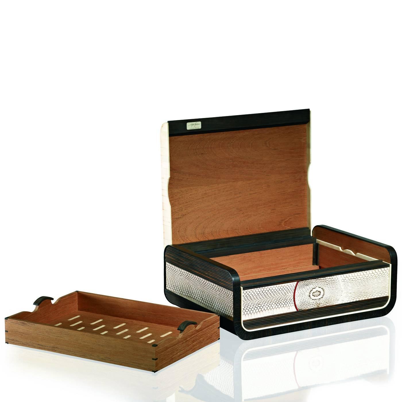 This elegant cigar box in ebony Macassar wood, with its distinctive dark brown stripes, is decorated with horn accents around its perimeter. The lid is linked to the box thanks to a zip in ebony wood decorated with iguana skin. Snake skin decorates