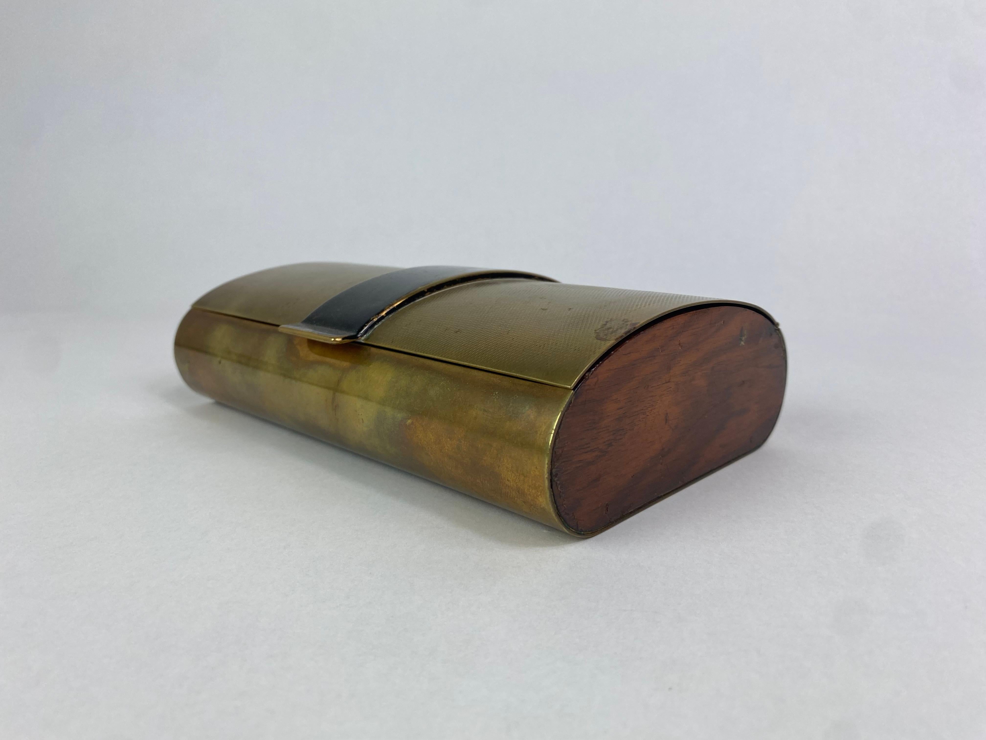 Brass and wooden cigarette box, designed by Carl Auböck, shows a beautiful guilloche top surface. The brass shows fine patina, enriched by the contrast of the wooden sides of the box. 
Listed as a scetch drawing in: 