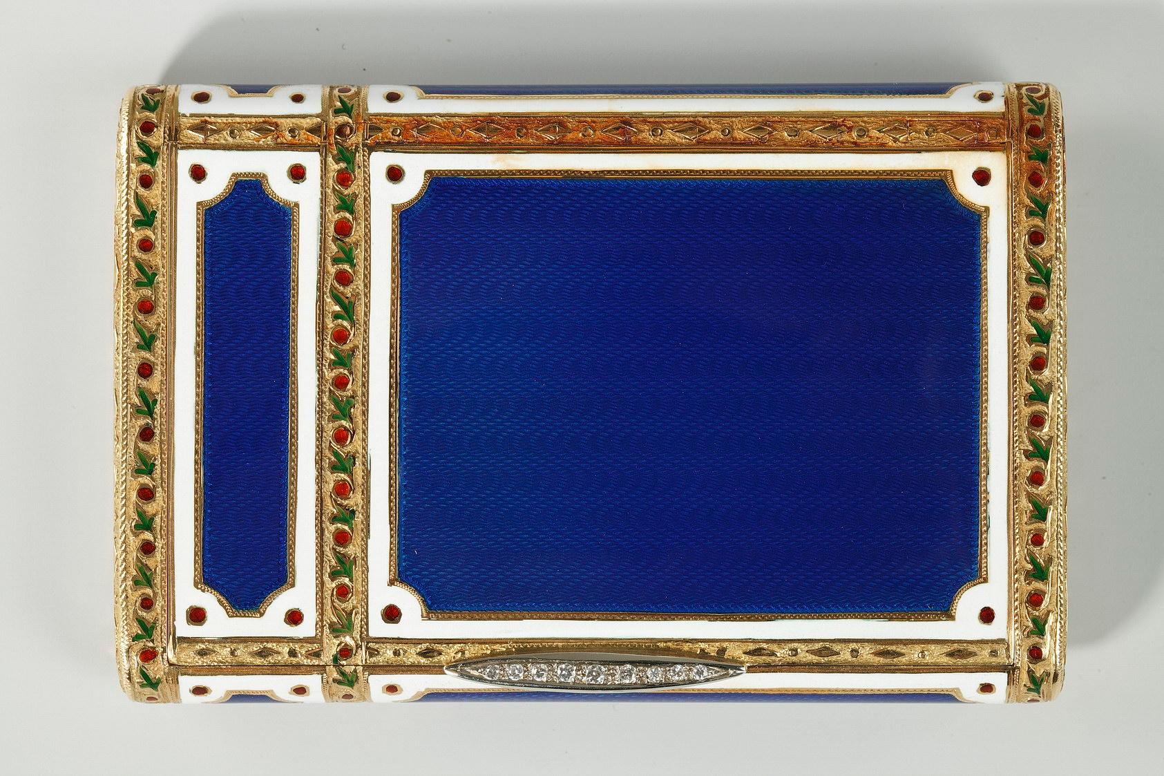 Large rectangular case in enameled gold. The panels of the case are embellished with translucent, royal blue enamel that reveals the intricate wave pattern in the gold underneath. Each panel is framed with a border of white enamel as well as a