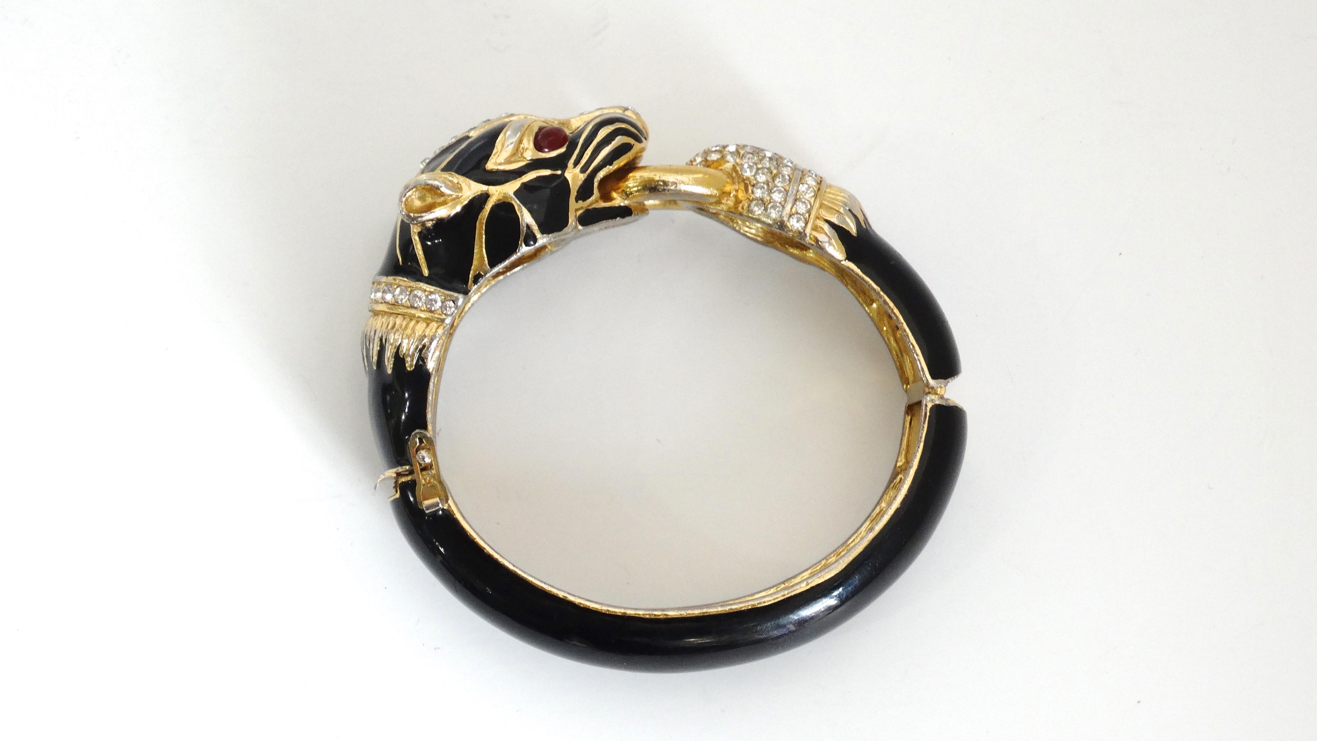 Spice up your bracelet game with this amazing Ciner bracelet! Circa 1970s, this Ciner gold plated bracelet is finished in a black enamel and features a detailed panther knocker decorated with red glass eyes and crystals. Hinge closure.The perfect