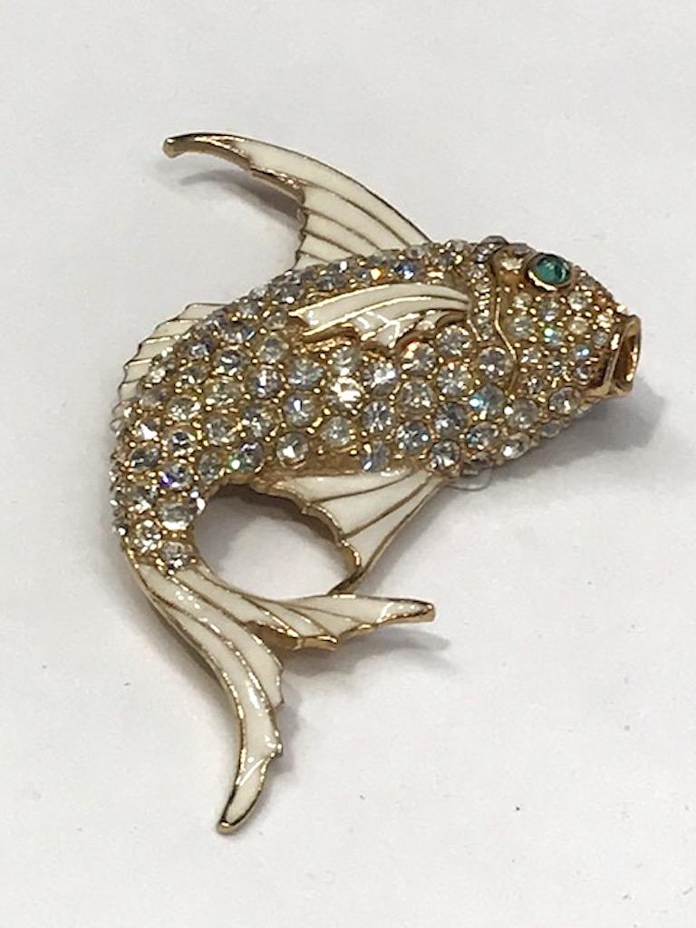 A stunning and beautifully crafted 1980s Ciner gold fish enamel brooch. The fins and tail are white enamel with the body set with rhinestones. The fish eye is a green glass cabochon. Very three dimensional with the fish in an upward swimming