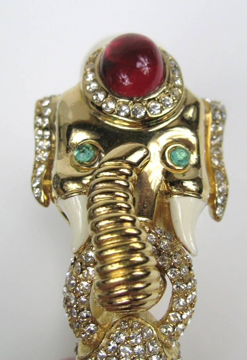 Ciner Elephant bangle. Features a mogul elephant that is set in a beige enamel. Has a faux Reddish stone and green eyes. The bangle also includes sparkling pave clear rhinestones. The hinged bracelet is secured with a safety clasp and a hinge