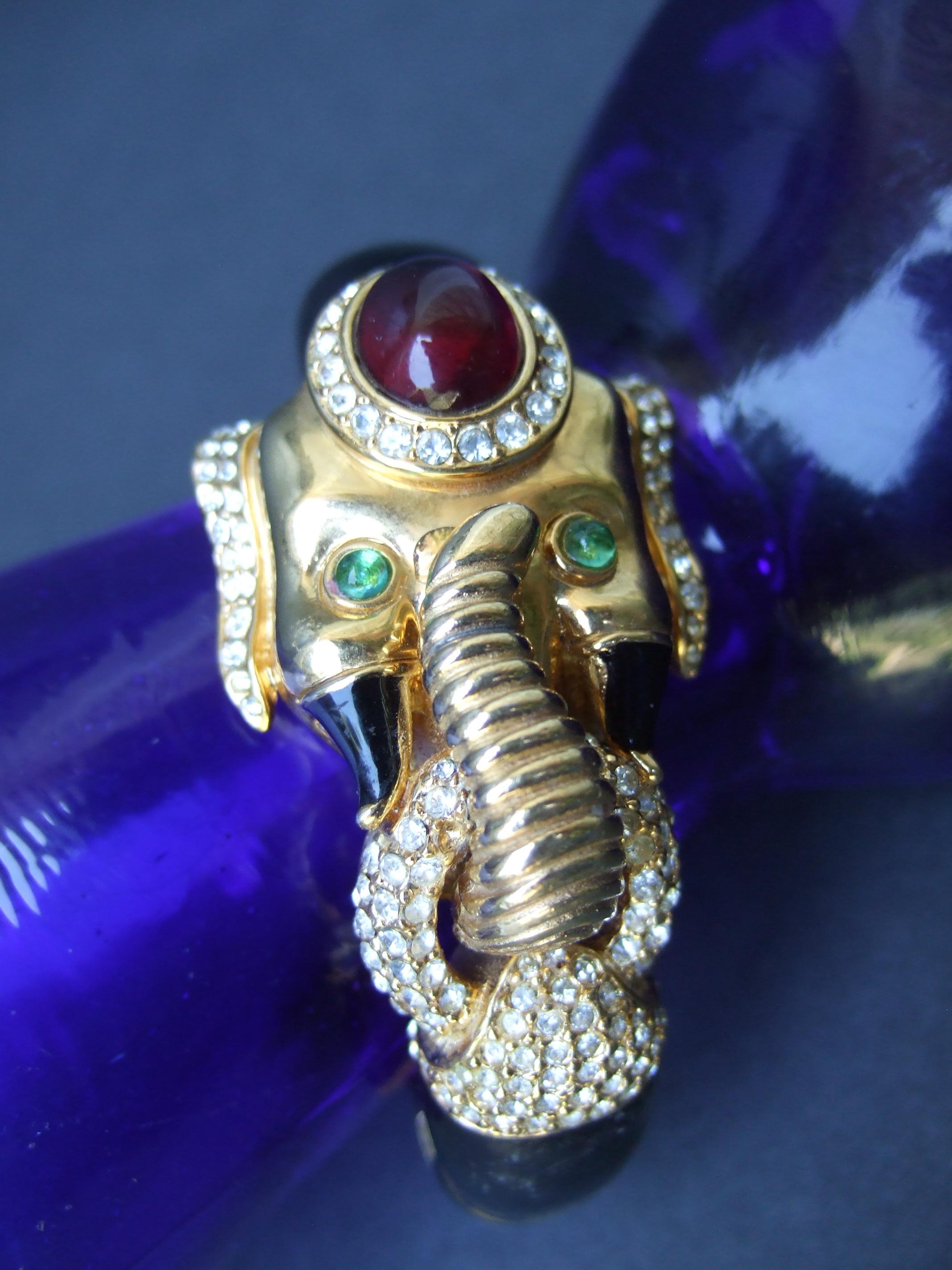 CINER gilt metal black enamel glass jeweled hinged elephant bracelet c 1970s
The opulent bracelet is designed with an exotic elephant adorned with a ruby color
glass cabochon mounted on top the head

Accented with green crystals eyes & clusters of