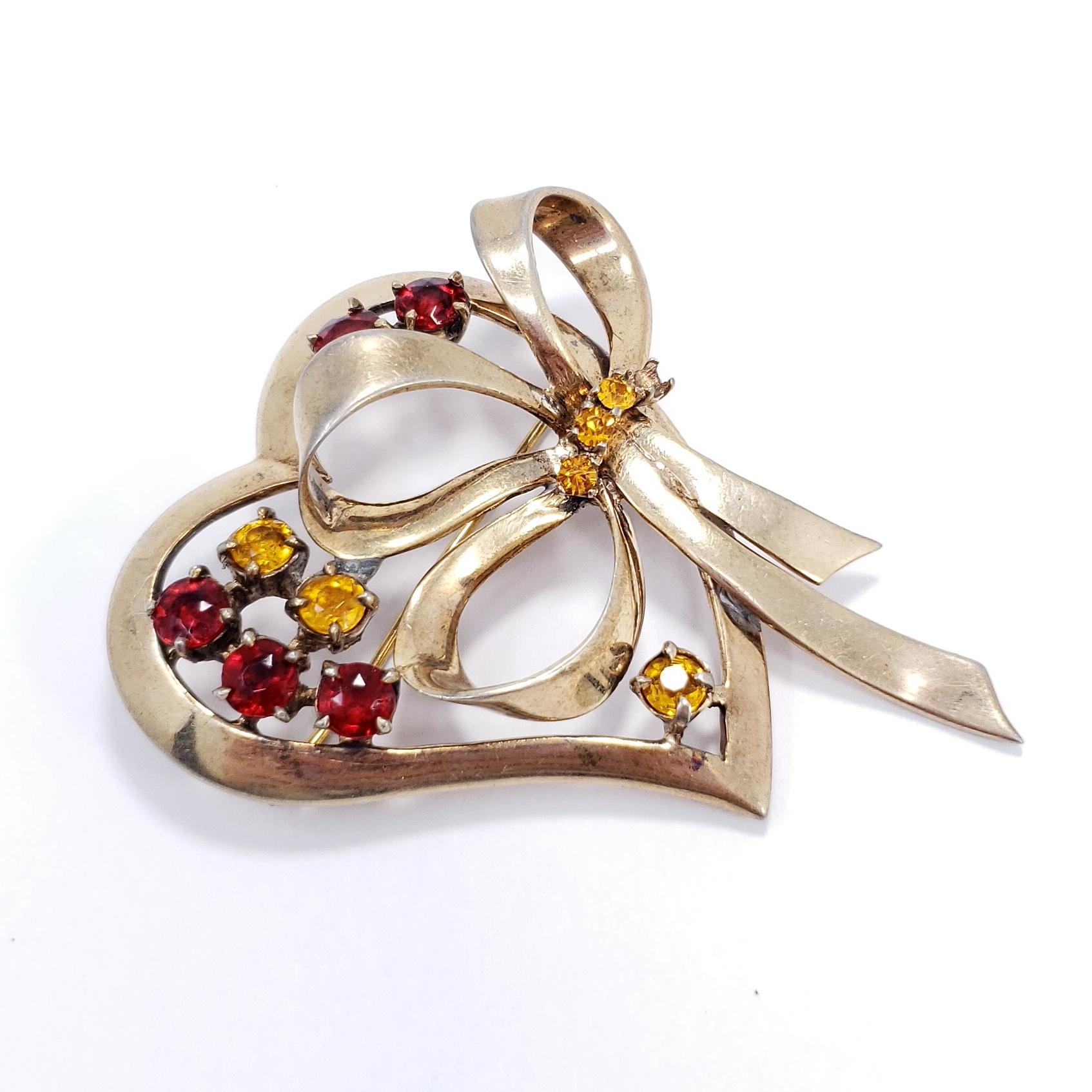 Stylish pin brooch from Ciner. Features a sterling silver, gold-plated heart and bow motif decorated with citrine and ruby-colored crystals.

Gold-plated sterling silver (vermeil).

Hallmarks: Ciner, Sterling

Good condition. Has been repaired.