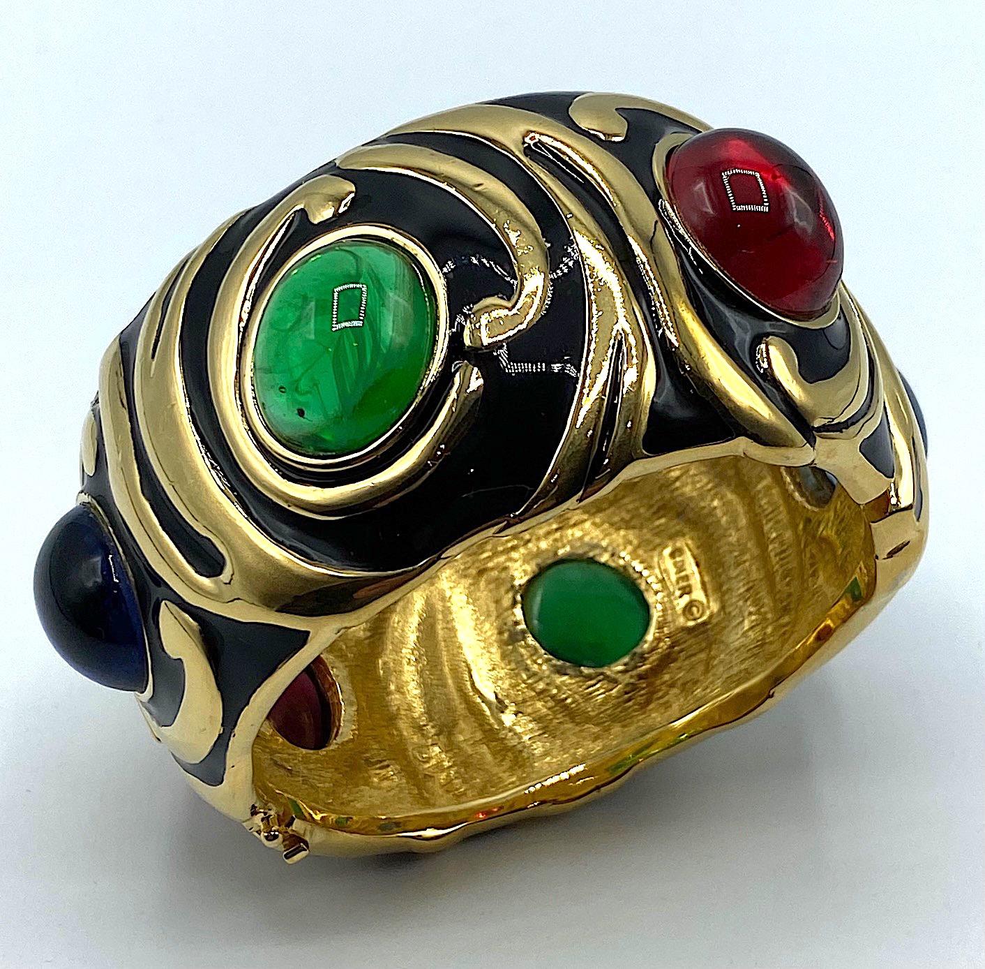 A stunning Ciner of New York bracelet from the 1980s. Beautifully black enameled on gold in a swirling pattern and set with six large red, blue and green .The green glass cabochons have streaks of white to emulate the inclusions in natural emeralds.