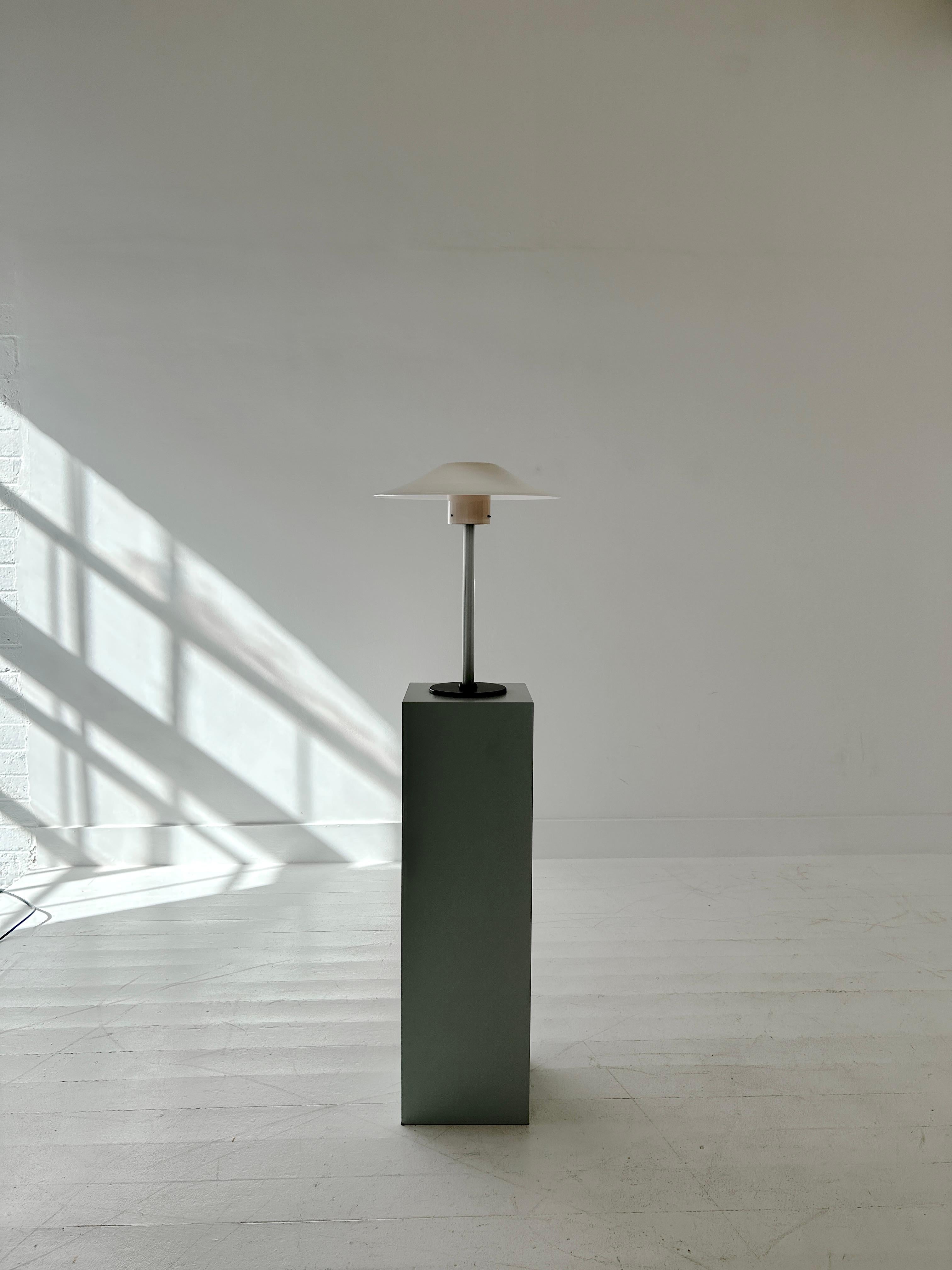 An elegant table lamp made from layered and blown Murano glass and a circular cast iron metal base. Signed.

A single piece of glass forms the shade, connecting to the fluted glass stem via three screws. Light emits through the opaline glass at the
