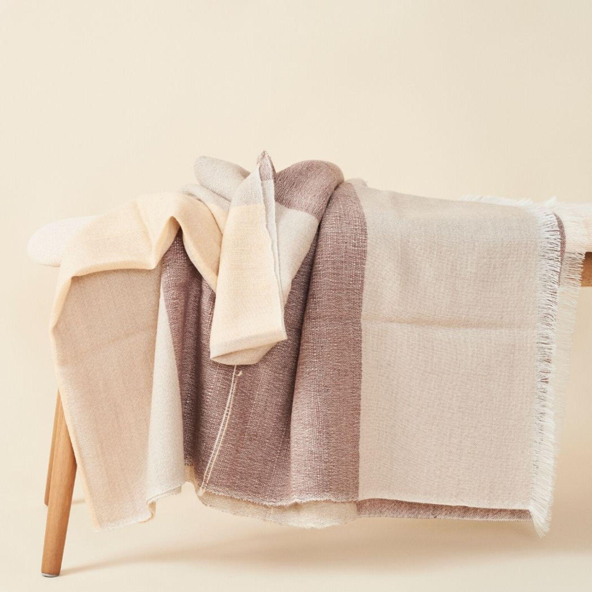 Die mit viel Liebe zum Detail handgewebte Decke Cino verbindet auf luxuriöse Weise den Wert des Erbes mit hochwertiger Handwerkskunst.  Das Design aus hochwertigem Merinogarn besteht aus farbigen Blockstreifen in neutralen Creme-, Beige- und