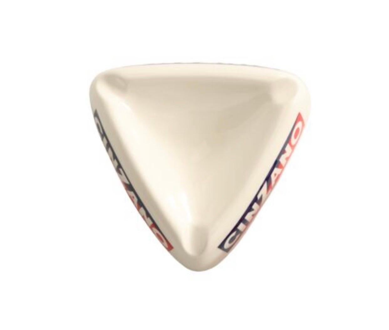 A triangular ceramic ashtray with the distinctive Cinzano logo in red, white and blue on all three sides, and a cigarette rest at each corner.
 