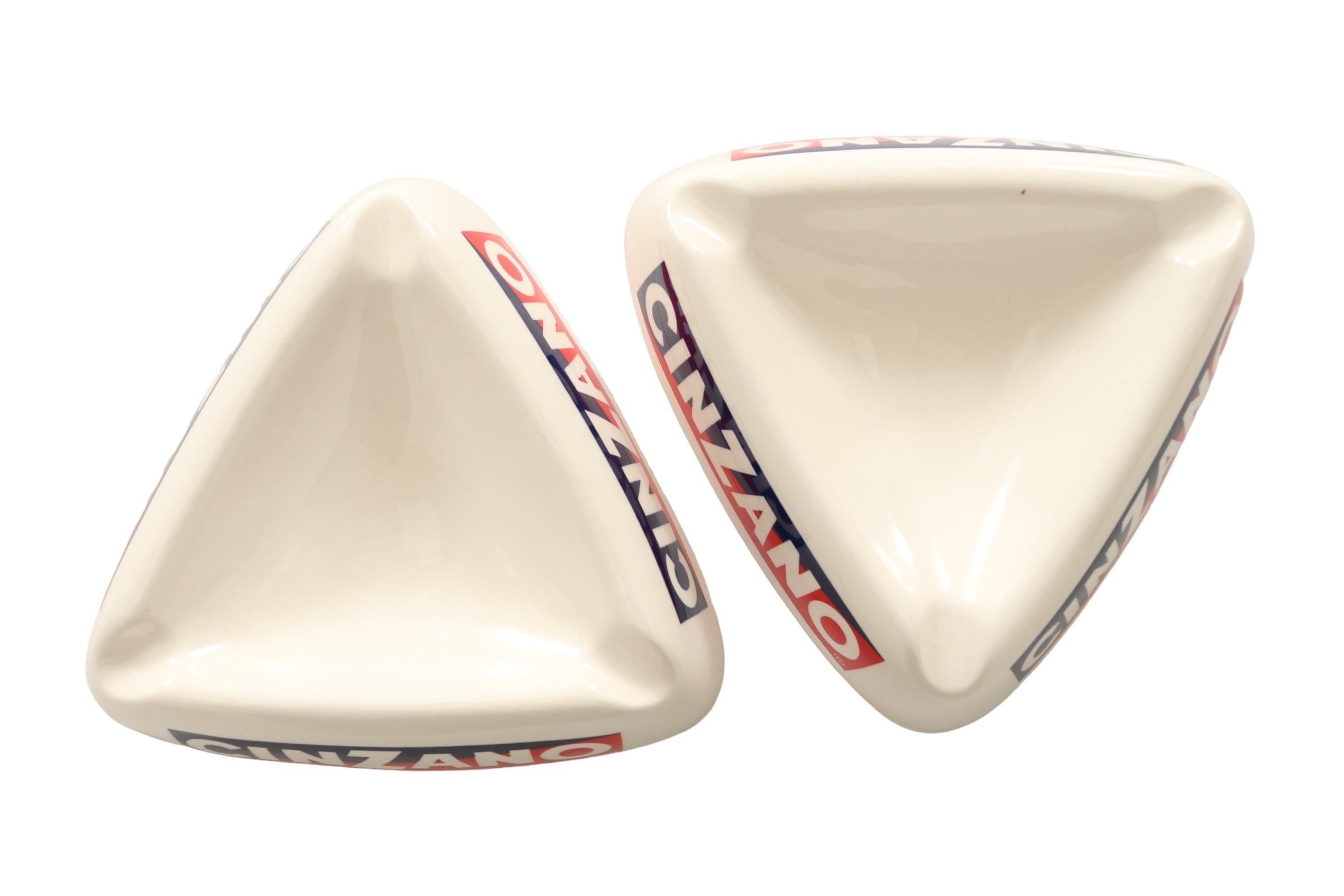 A pair of triangular ceramic ashtrays with the distinctive Cinzano logo in red, white and blue on all three sides, and a cigarette rest at each corner. Dimensions per ashtray.
 