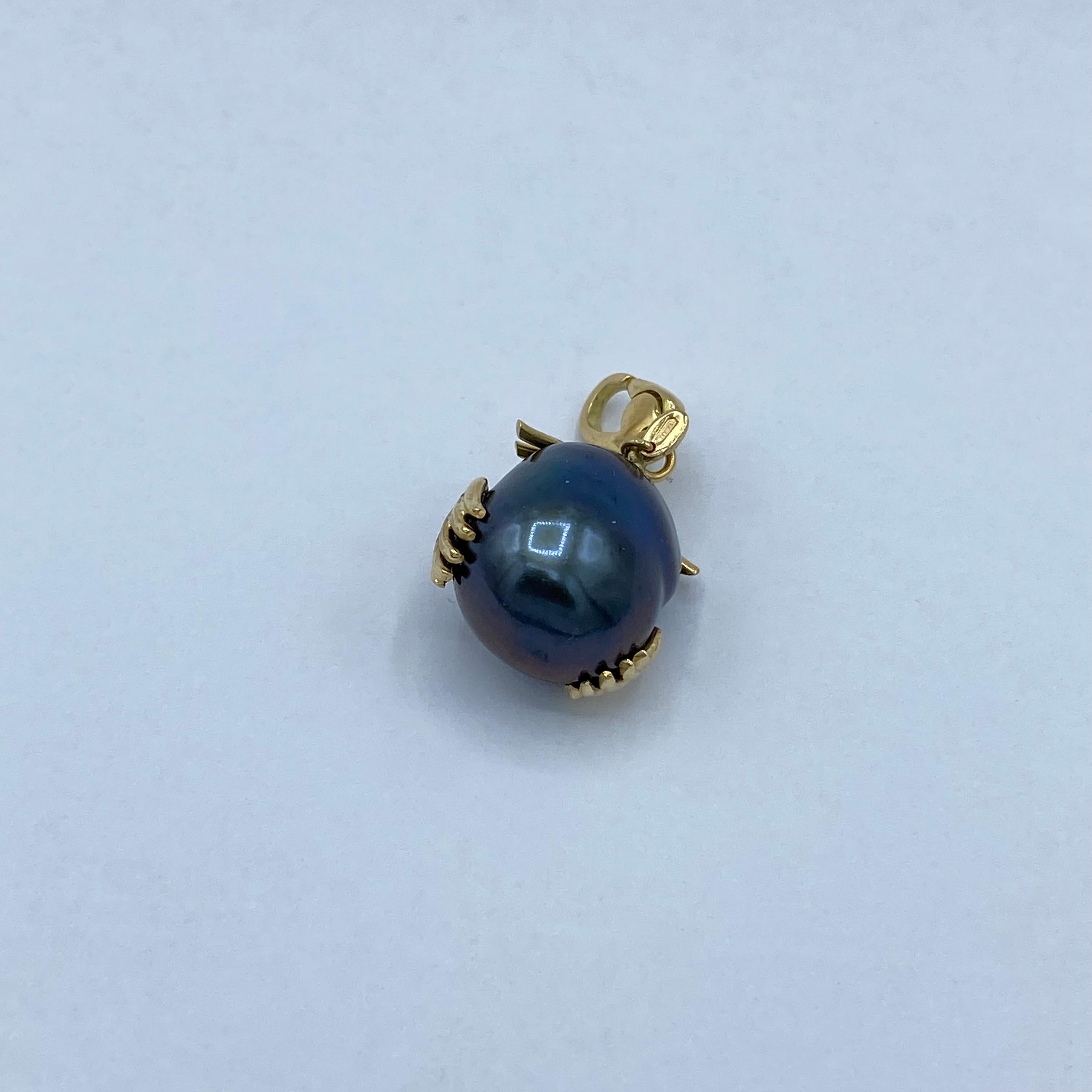 A small lucky owl born from a dark gray South Sea pearl with green/blue highlights (the color of this pearl has not been treated). 
Using 18Kt yellow gold wire, I made the parts that complete the owl: the eyebrow, the beak, the eyes and the two