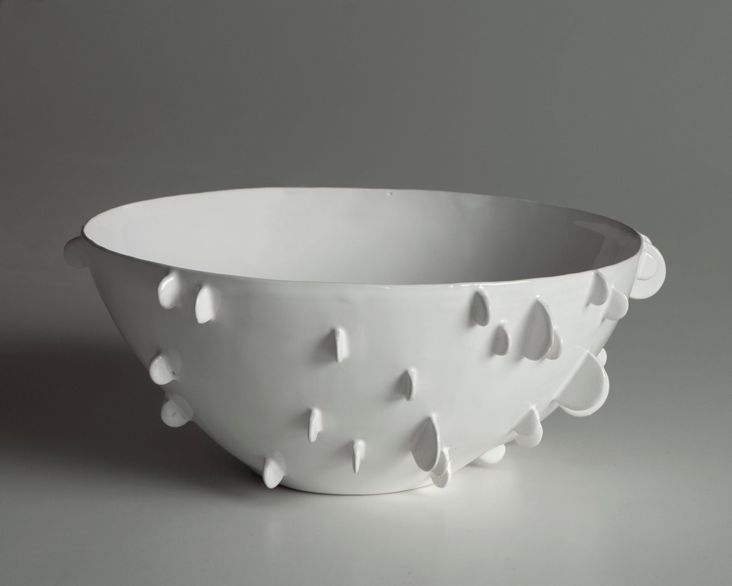 La ciotola in ceramica bianca presenta un delicato motivo a rilievo che evoca l'effetto dei petali. La smaltatura, applicata con tecnica a immersione, conferisce un carattere unico alla superficie, evidenziando le sottili imperfezioni che