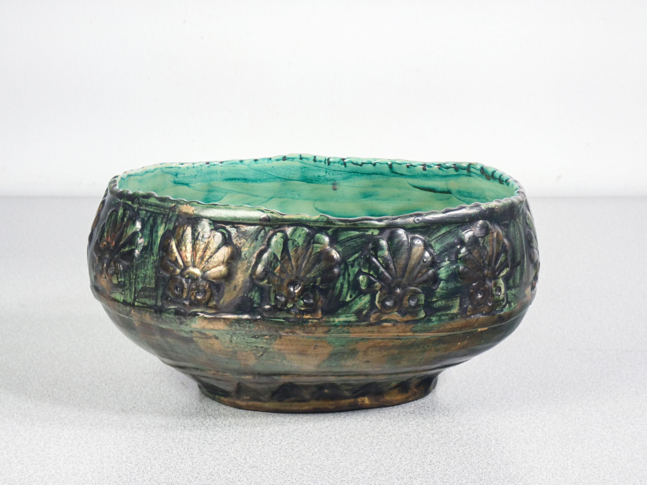 Decorative painted ceramic bowl with glazed finish. The outer surface features a relief pattern of stylized shells or flowers, with a texture reminiscent of organic or natural decorations. The outer coloring is predominantly dark green and bronze,