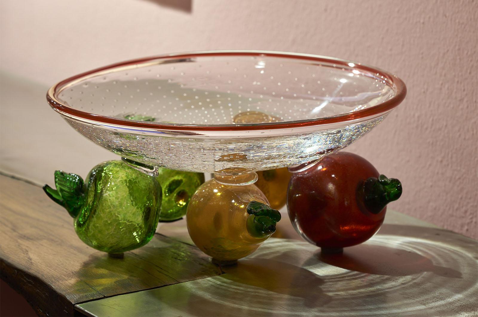 Obstschale aus Glas, entworfen von Borek Sipek für Ajeto im Jahr 1992.
Die obere Schale ist komplett handgefertigt und ruht auf bunten Dekorelementen, die an Obstformen erinnern. Die Oberfläche der oberen Platte ist auf der Innenseite glatt und auf