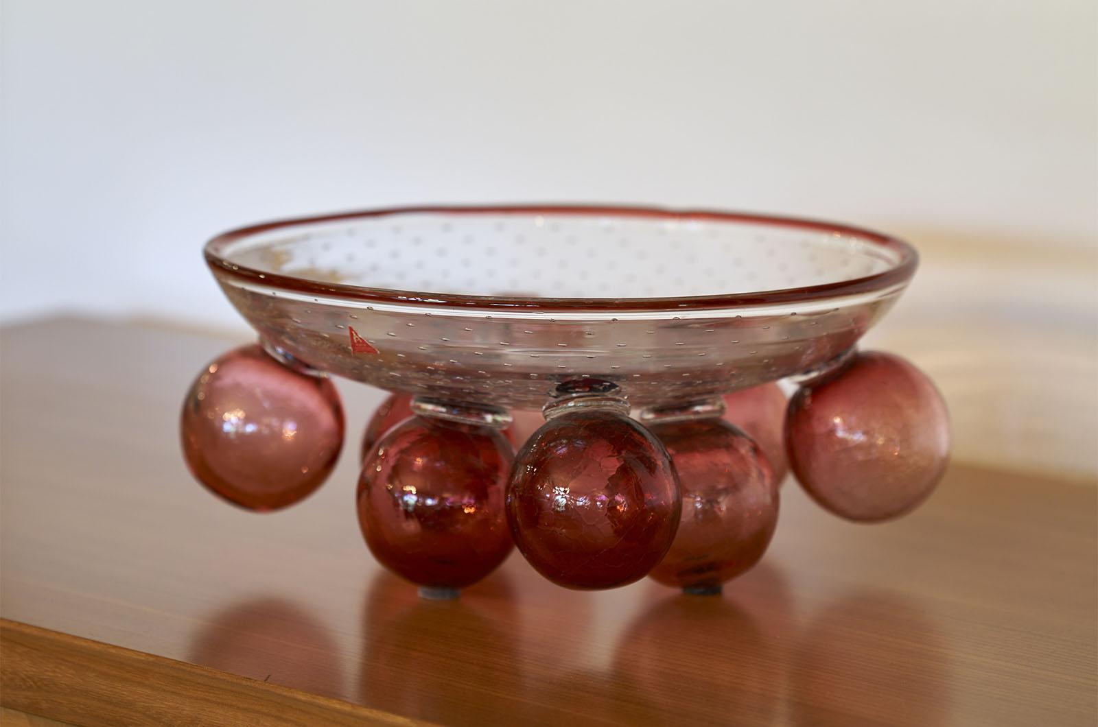 Obstschale aus Glas, entworfen von Borek Sipek für Ajeto im Jahr 1992.
Die vollständig handgefertigte obere Schale ruht auf bunten Dekorelementen, die an Kugeln erinnern. Die Oberfläche der oberen Platte ist auf der Innenseite glatt und auf der