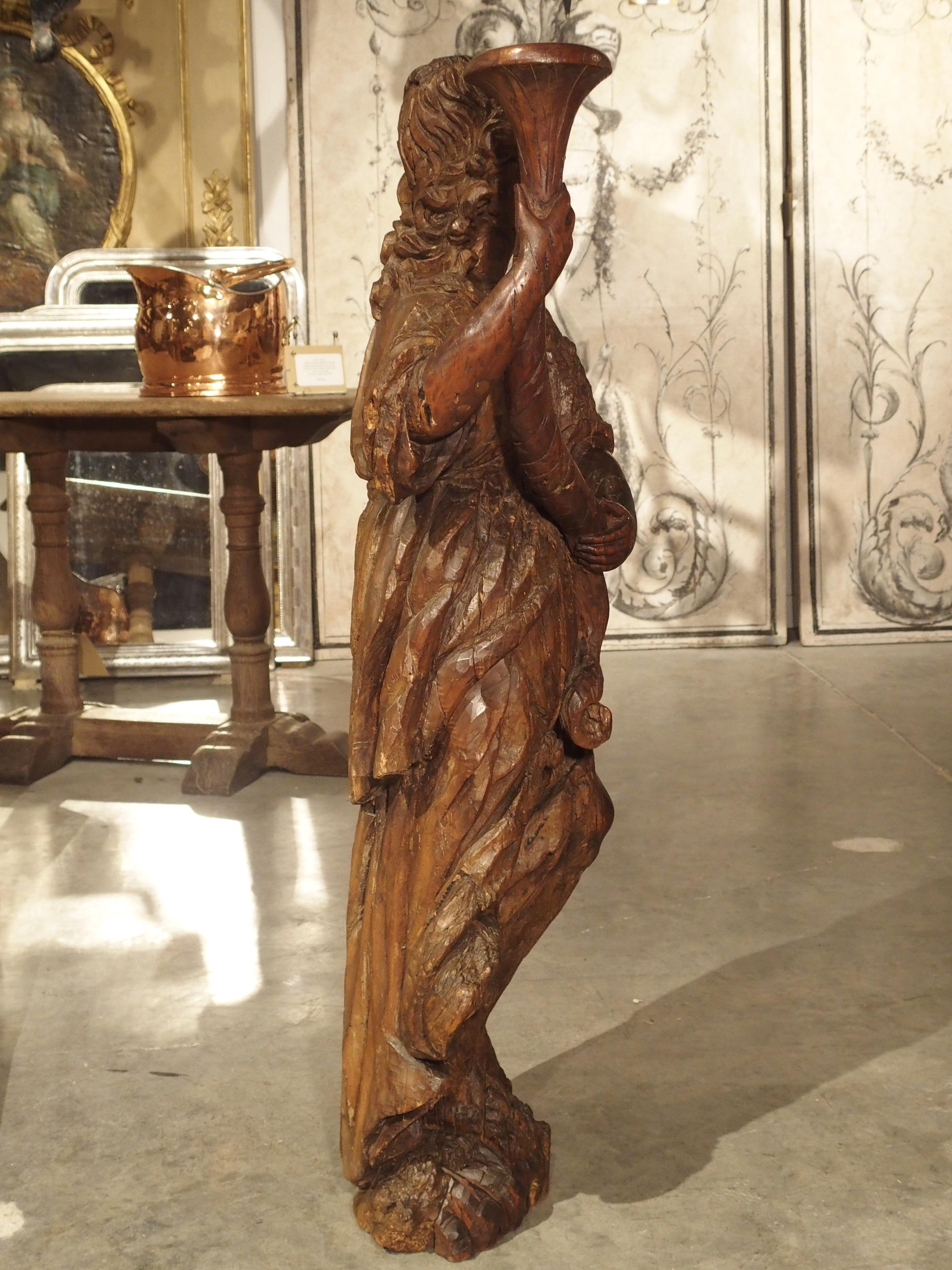 This remarkable carved wooden statue is approximately 380 years old and was carved from Italian Rovere or Durmast wood. This is a variety of European oak known for its tough and heavy nature. The statue depicts a robed figure holding a cornucopia