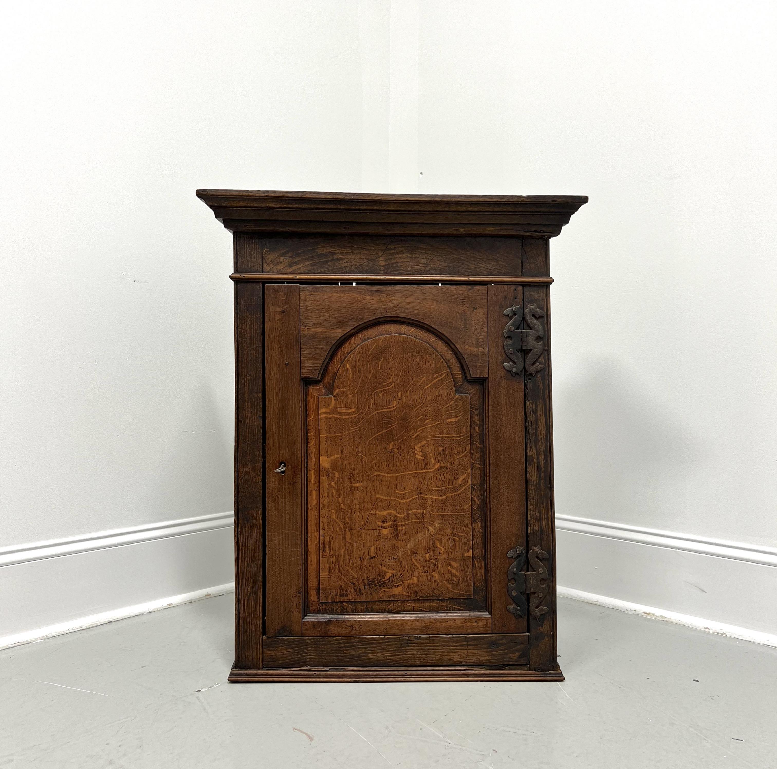 An antique Chippendale style hanging cupboard, unbranded. Handcrafted of quartersawn oak with crown molding to the top, a tombstone panel door, serpentine shaped brass hinge hardware, an ogee edge to the base, and metal wall hangers attached to the