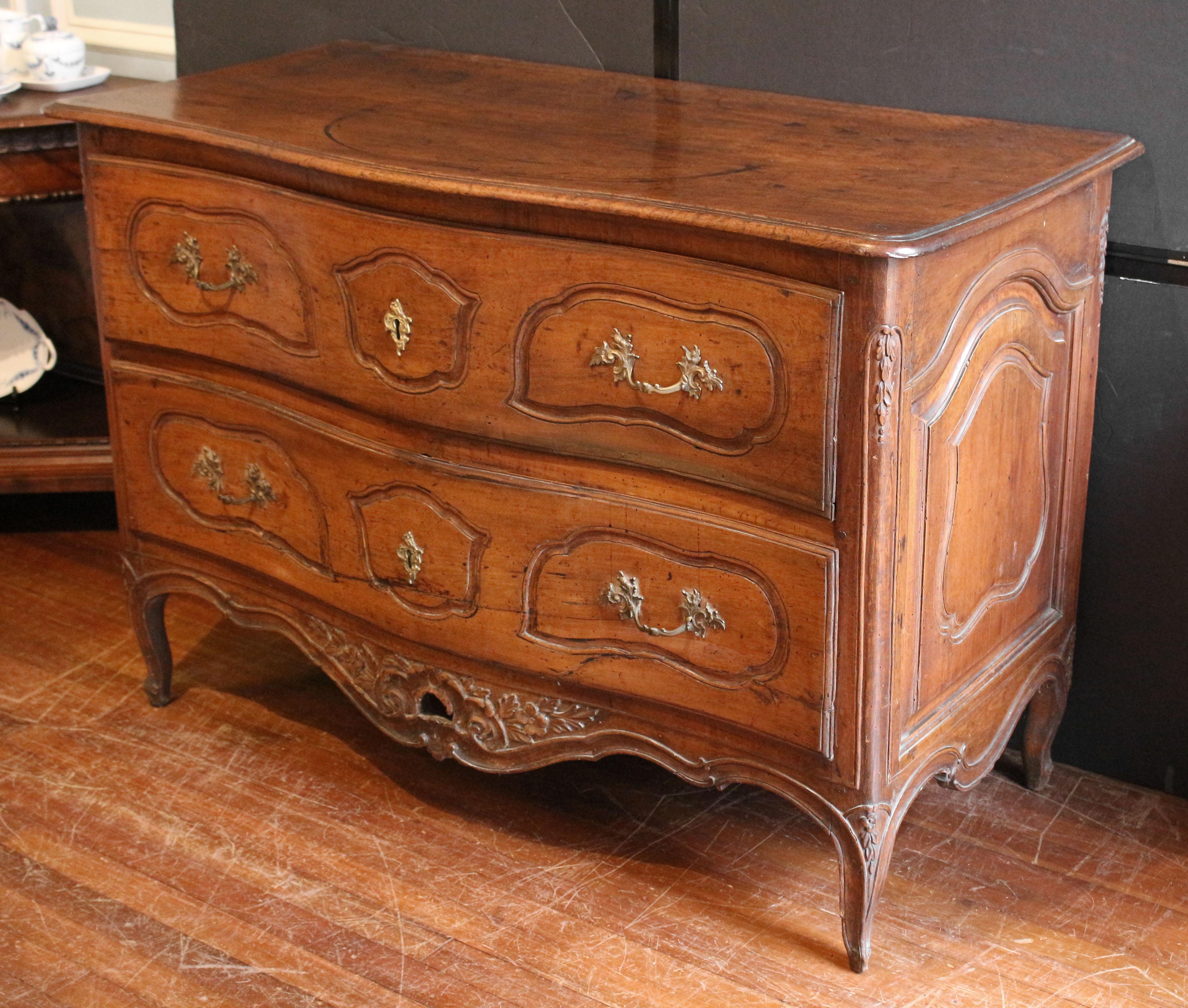 Circa 1735-55 French Rococo period commode from Provence. Walnut. Serpentine front; two drawers with triple asymmetrical shaped, molded cartouches; pierced, carved apron ending in well molded edge; raised on short floral carved cabriole legs ending