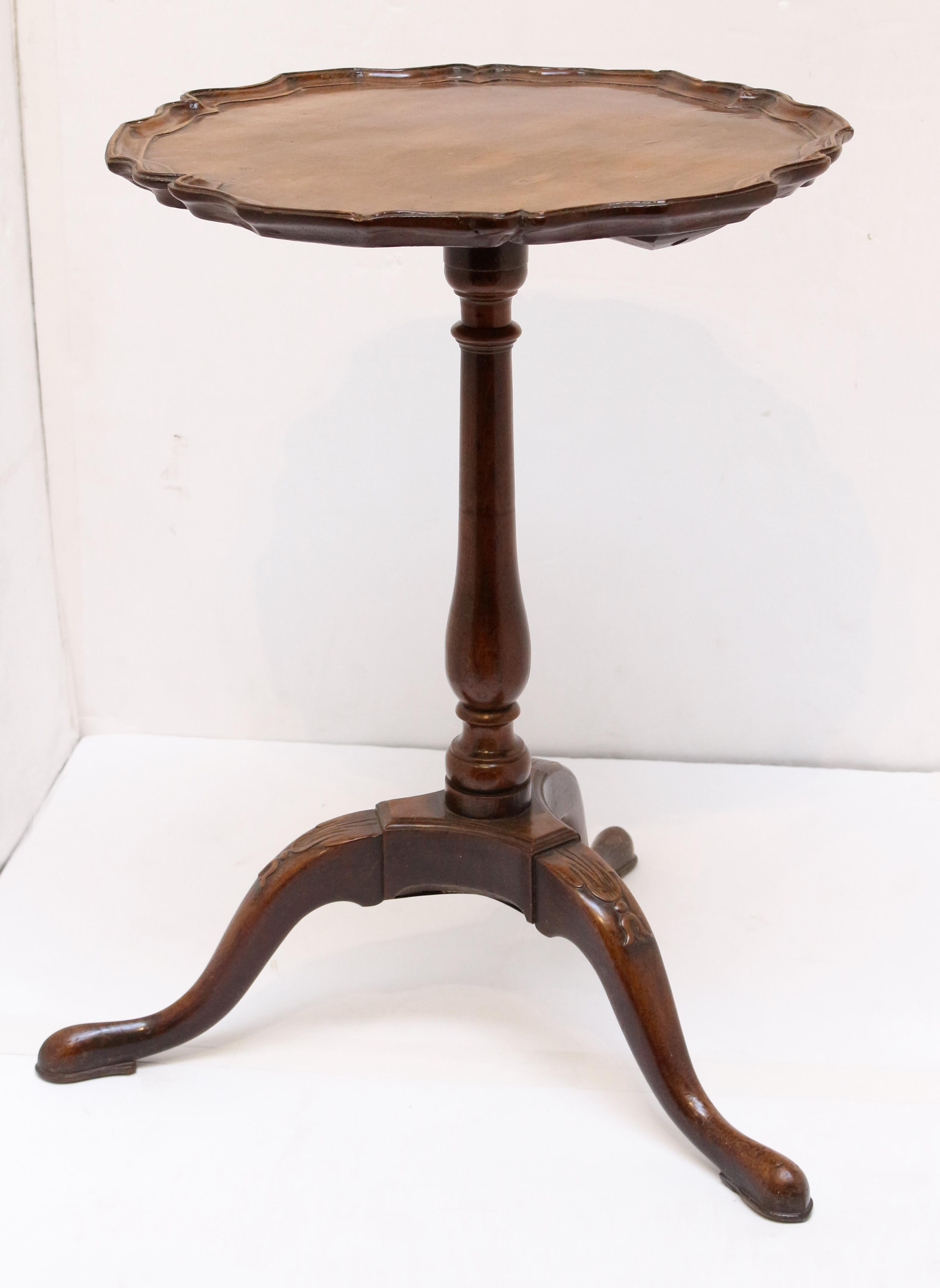 Circa 1760 George III period candlestand table, English. Mahogany. Well shaped and desirable piecrust top. Delicately turned vasi-form shaft with ring carved accents. Tripod base with leaf & bellflower carving at the knees gracefully sloping down to
