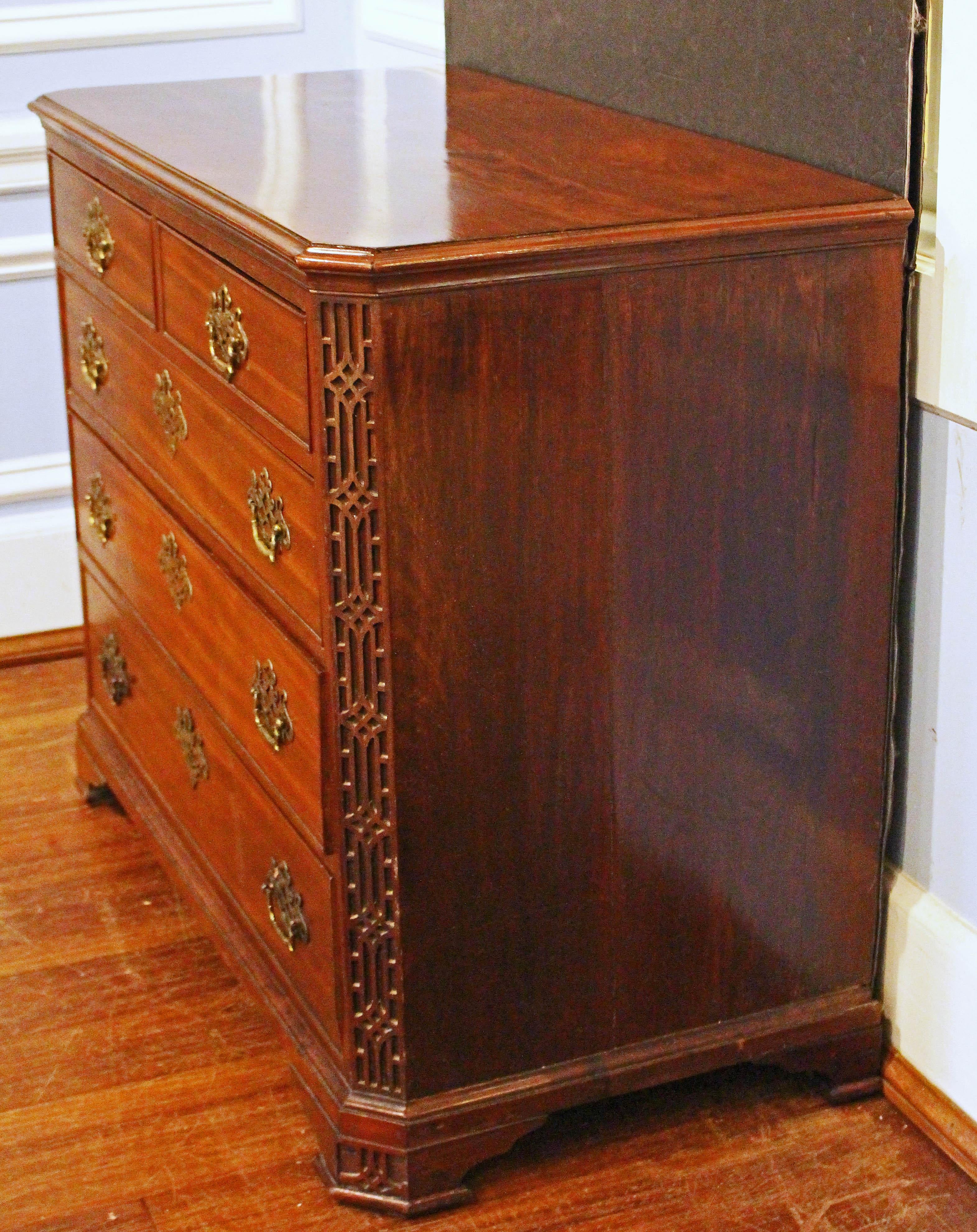 Circa 1765-80 George III period chest of drawers, English. Canted corners with blind fretwork which extends through the bracket feet. Mahogany with oak secondary wood. 2 short over 3 long drawers. Well molded top. Superb quality original pierced