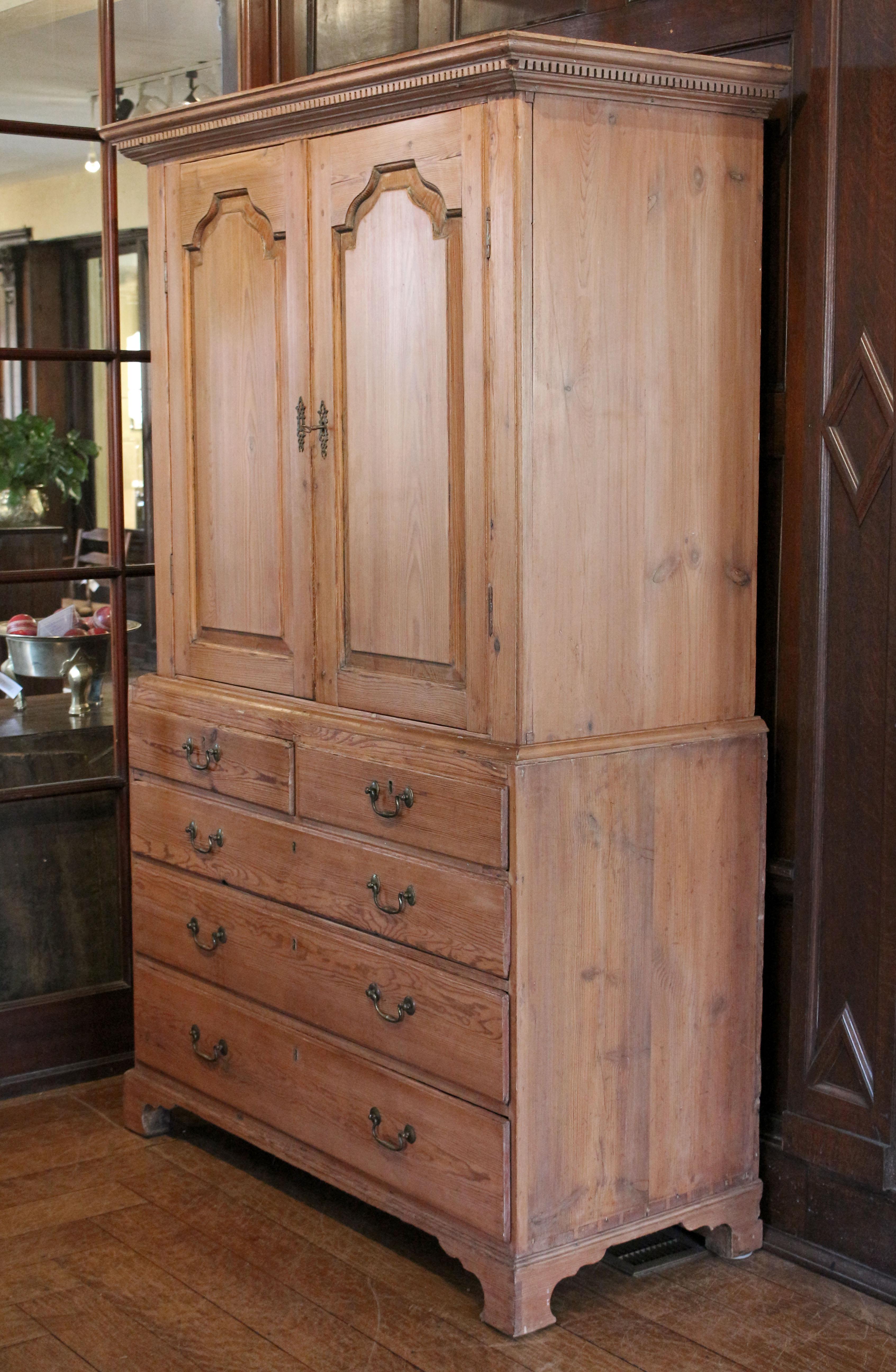Circa 1765-80 George III period linen press, English. Stripped Scotts pine with tombstone panelled doors, dentil molding on the integral crown, bail & rosette pulls, and raised on original bracket feet. Interior with 2 stationary shelves. Doors with