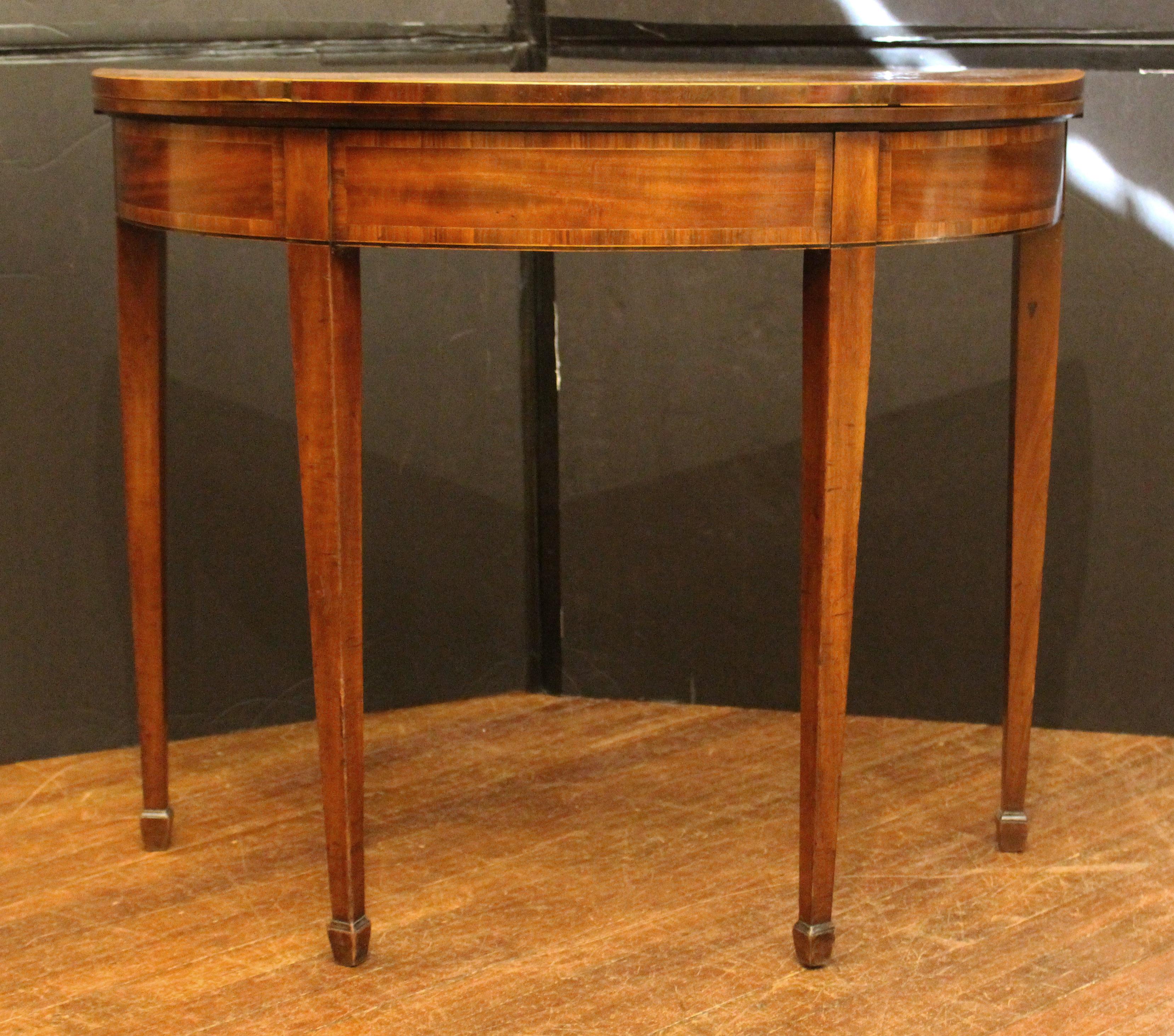 Circa 1780 George III demilune games table, English. Neoclassical. Well figured mahogany top and aprong sections each crossbanded with zebra wood and satinwood stringing. Lines of boxwood & ebony line the apron edge. Straight, tapered legs ending in