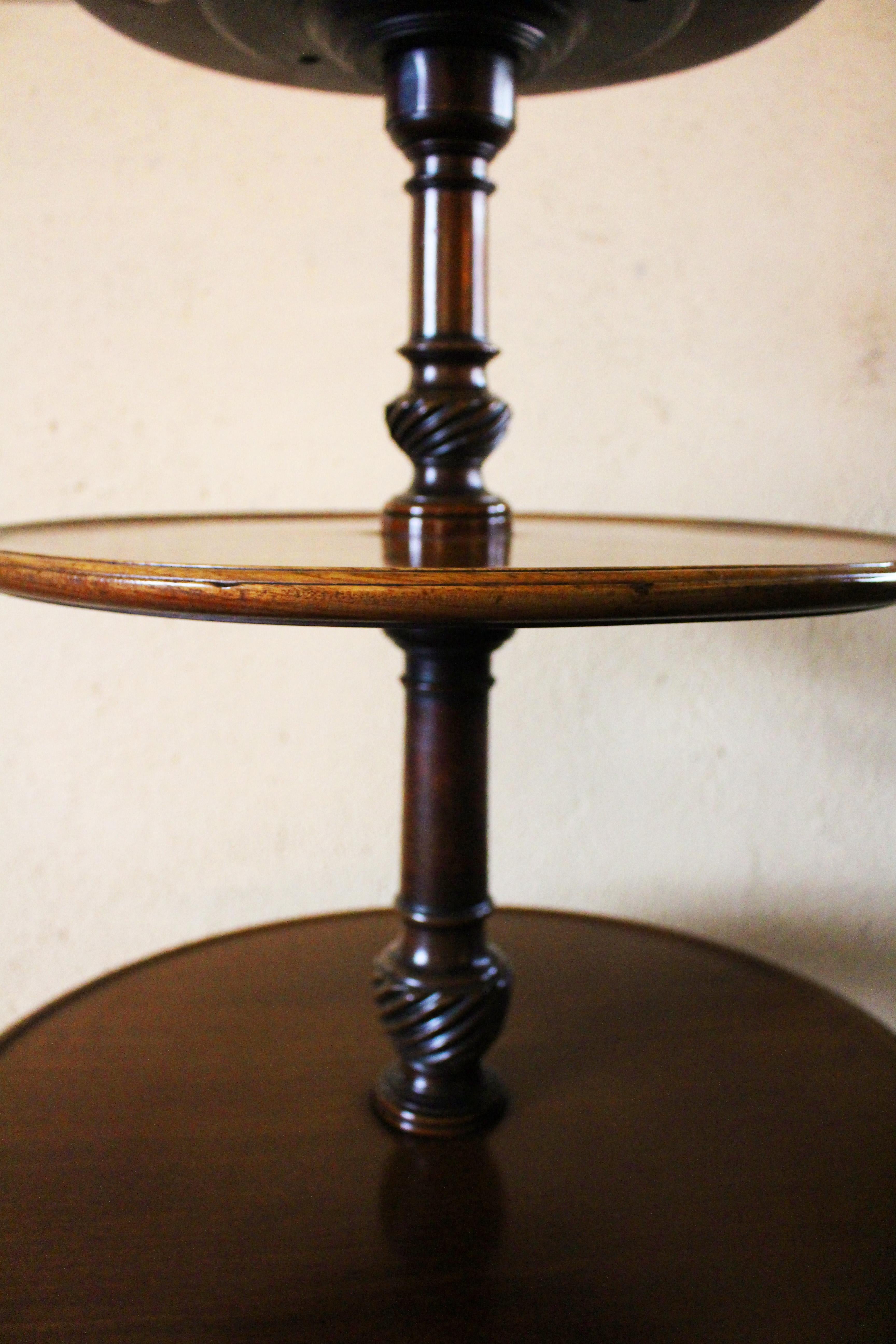 Circa 1780 Dumbwaiter, English, George III. Great color & form. Fine faded island mahogany. Each standard is carved with a swirled urn. Raised on tripod base, the snake feet with inset casters. Rotating shelves. Provenance: George Smith Antiques,