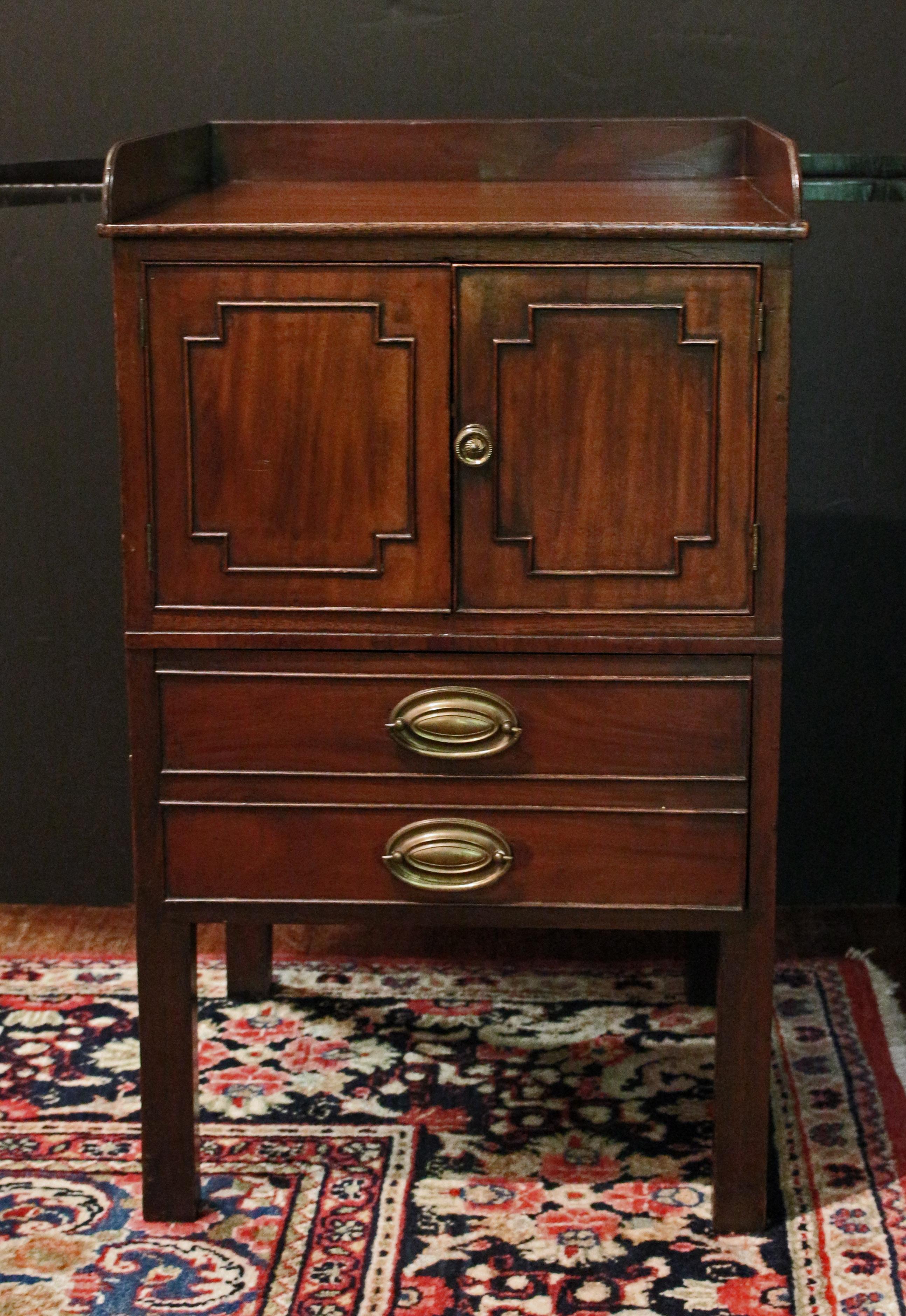 circa 1785 commode cabinet, George III, English. Mahogany & mahogany veneers. Gallery top. Converted from a bedside commode, now a cabinet over a deep drawer appearing as two drawers. Cut corner panelled doors. 32.5