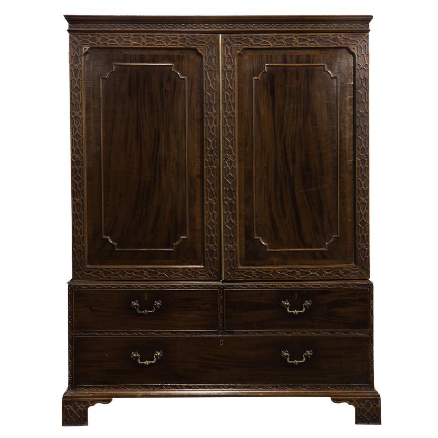 Late 18th Century George III mahogany linen press circa 1790, executed in the Chinese Chippendale taste, the carved and panelled double doors opening to five slide out shelves, above the three drawer lower case, and rising on carved bracket feet