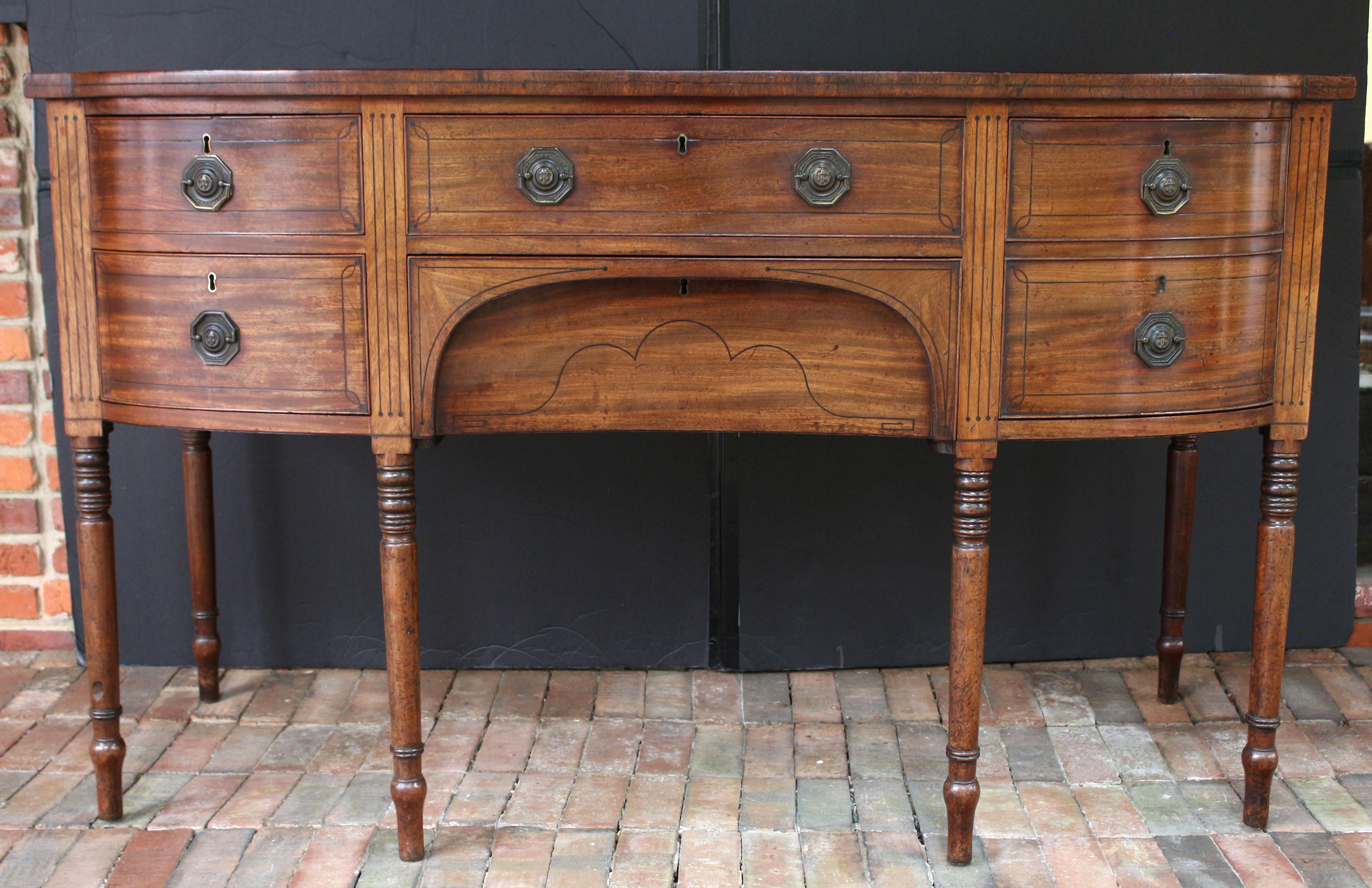 Circa 1800 Sheraton bowfront sideboard, English. Mahogany with decorative ebony line inlays across the drawer fronts, top edge, and surmounting each leg. Comprised of two long central drawer, one appearing as an apron, flanked by a deep drawer