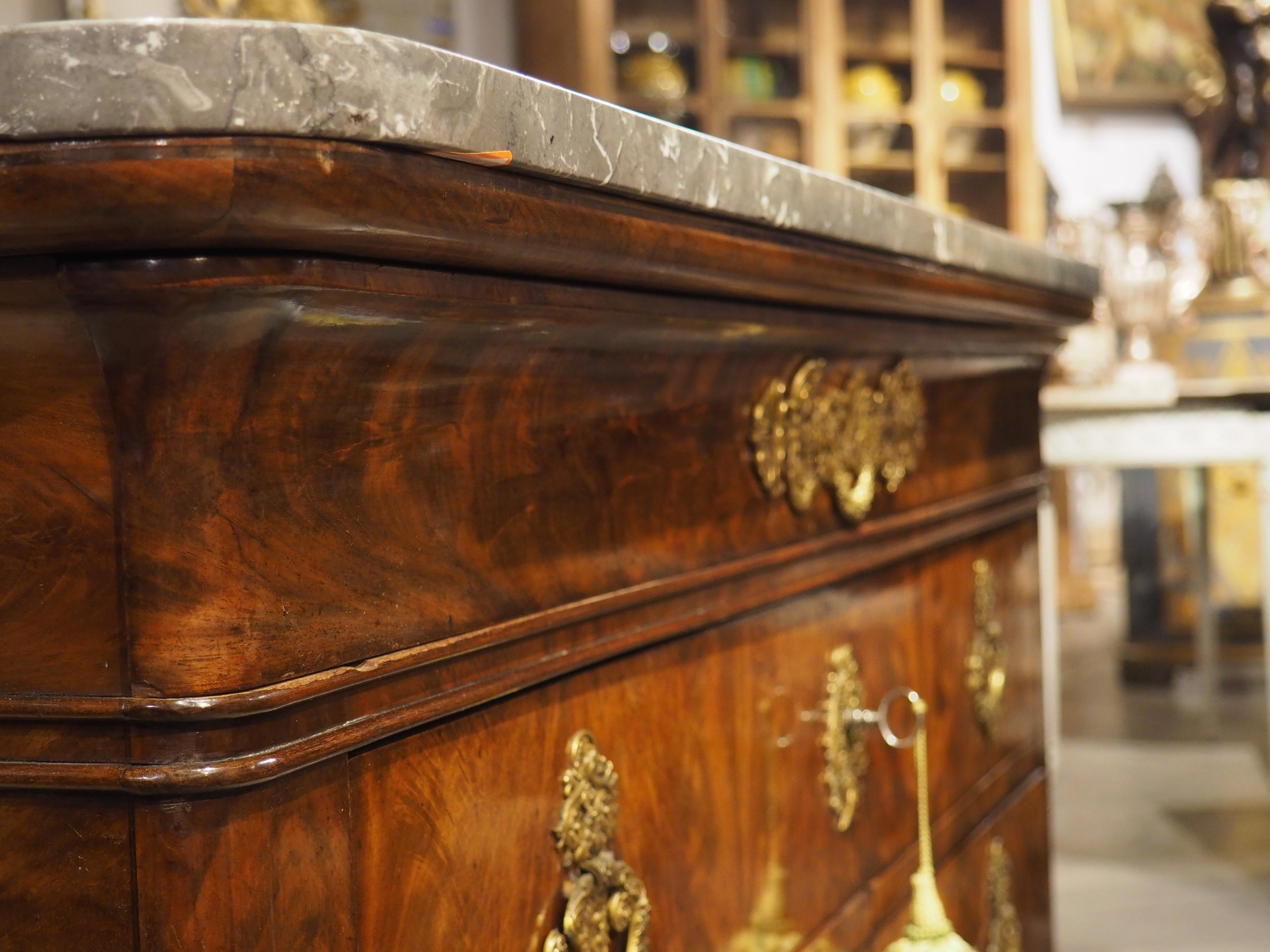 Topped by a one-inch thick marble top, this commode has a beautiful mahogany veneer with flame graining and foliate and floral gilt bronze hardware. Hand-carved in France, circa 1820, the stunning chest of drawers is from the Restauration period,