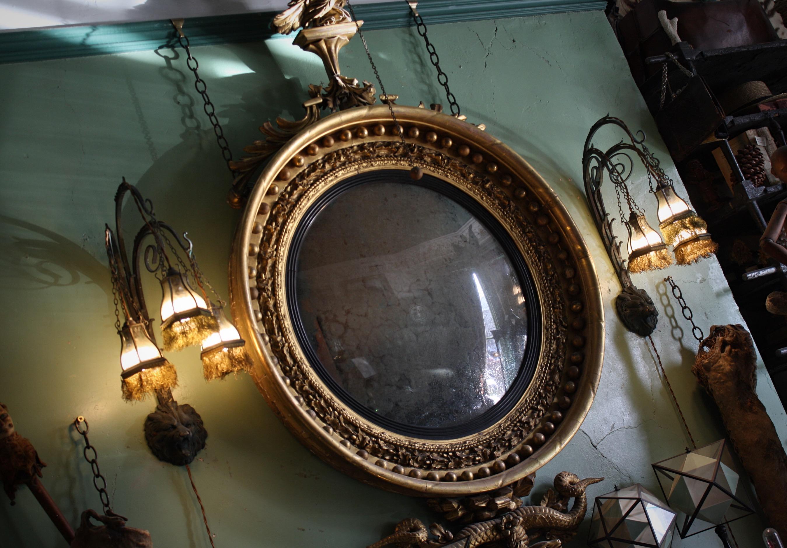 A circa 1820 Regency gilt convex mirror of grand proportions and typically form.

Ebonised reeded slip, applied gilt spheres and surmounted by an eagle perched with its wings spread holding a ball and chain.

The bottom of the mirror is