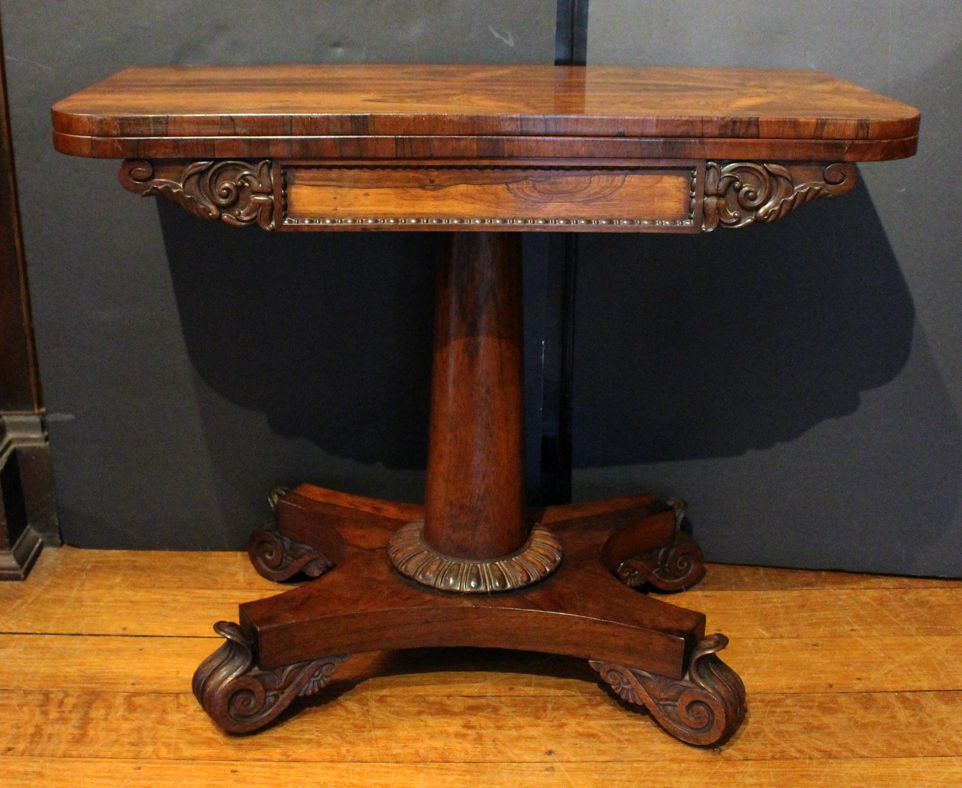 Circa 1825 swivel top card table, English. George IV period. Well figured rosewood. The apron with cenral frieze with bold egg & dart border and flanked by robust naturalistic carving. Raised on a reverse tapered turned upright ending heavy