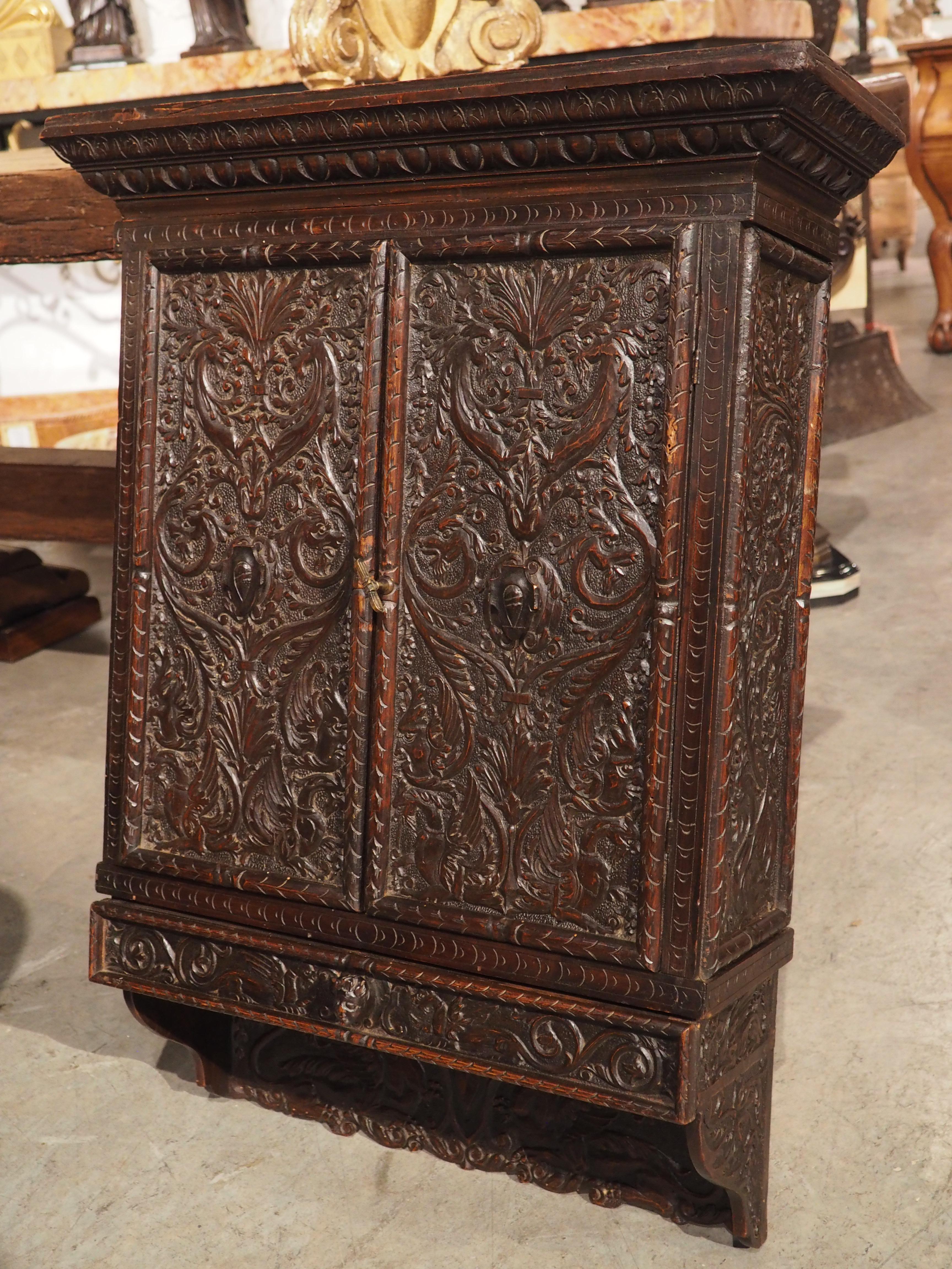 Hand-carved in Italy, circa 1830, this walnut wall cabinet has numerous Renaissance style motifs. The details are quite amazing, with all available space utilized. Even the edges of the two full length shelves have been adorned with recessed niches