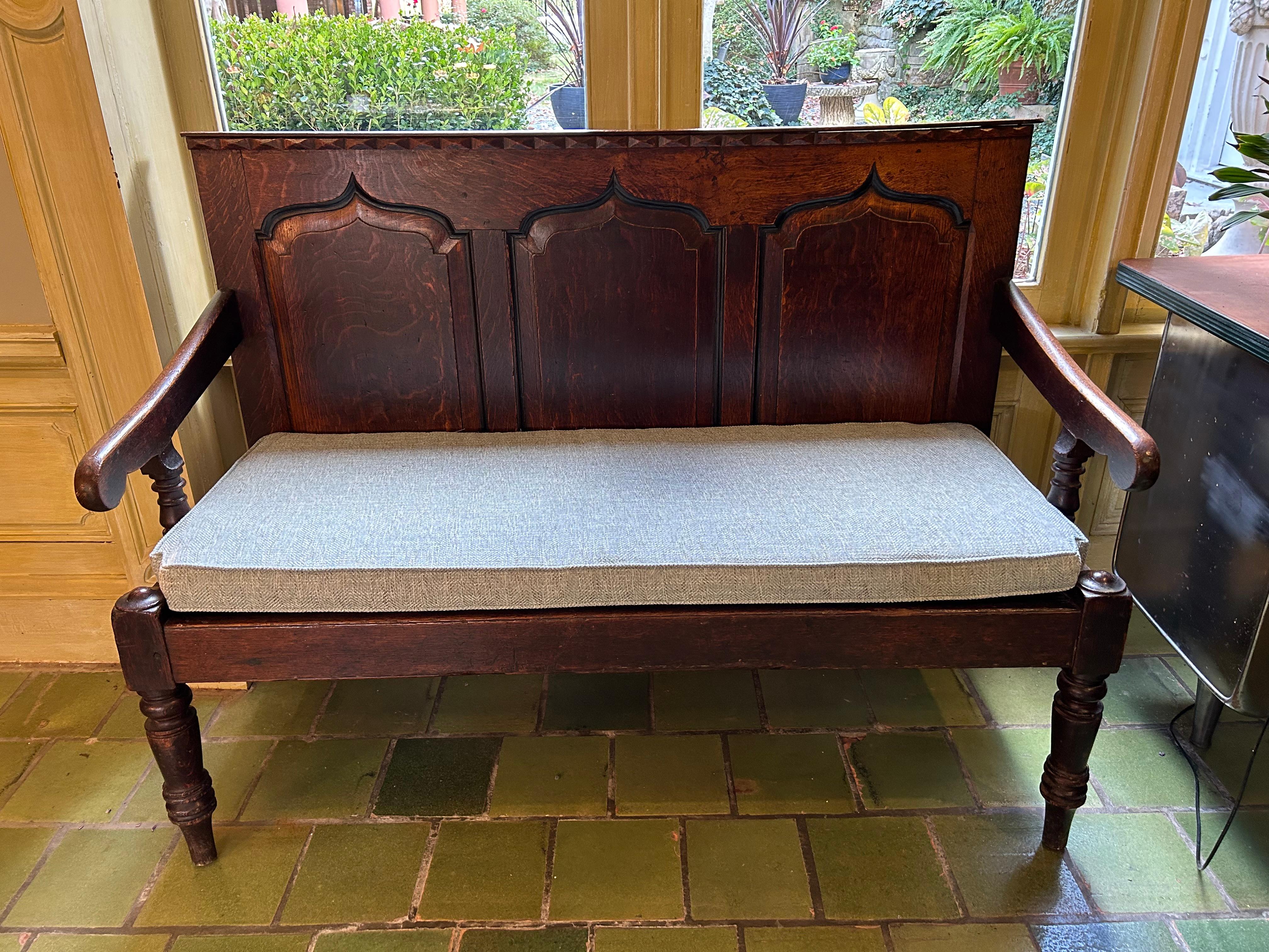 Circa 1830s Gothic influence settle bench, English, oak. Gothic style back with triple floating panels under a row of pointed rectangles. Raised on chunky turned, tapered & ring carved legs. Old loss at the end of one arm support upright. Wear
