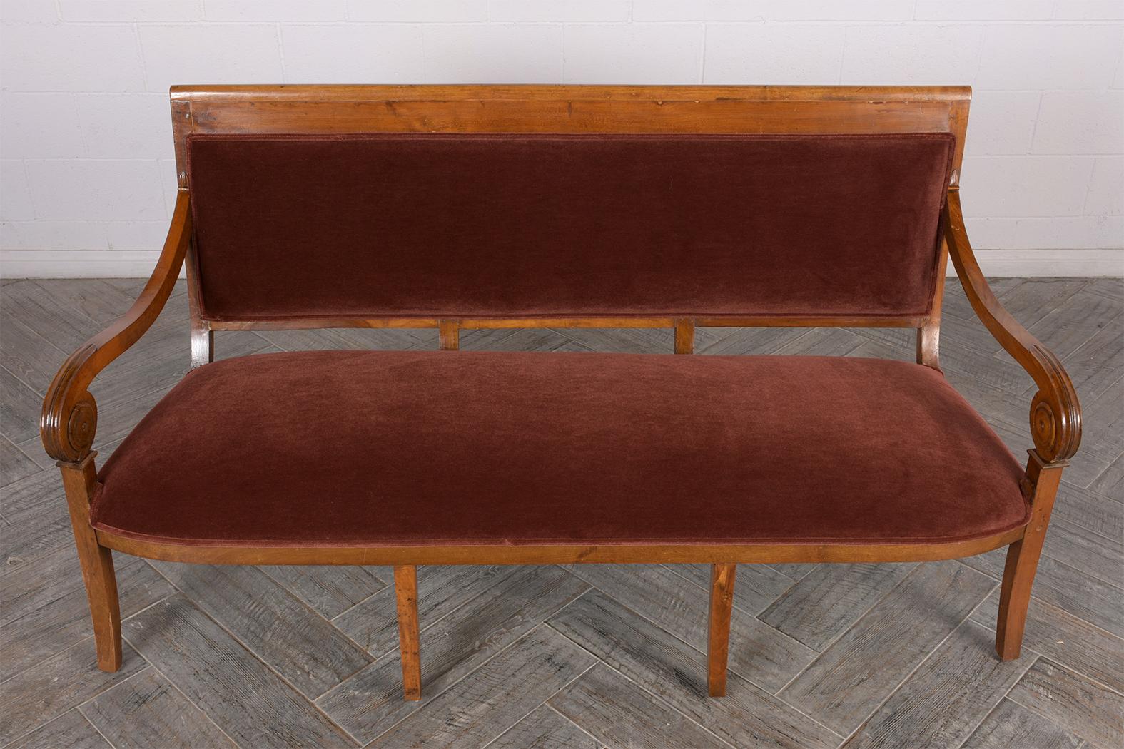 This French circa 1830s Empire Style Sofa bench has been completely restored. The carved frame is made of solid walnut wood finished in its original light walnut and patina finish. The frame features curved scroll armrests and two rows or four