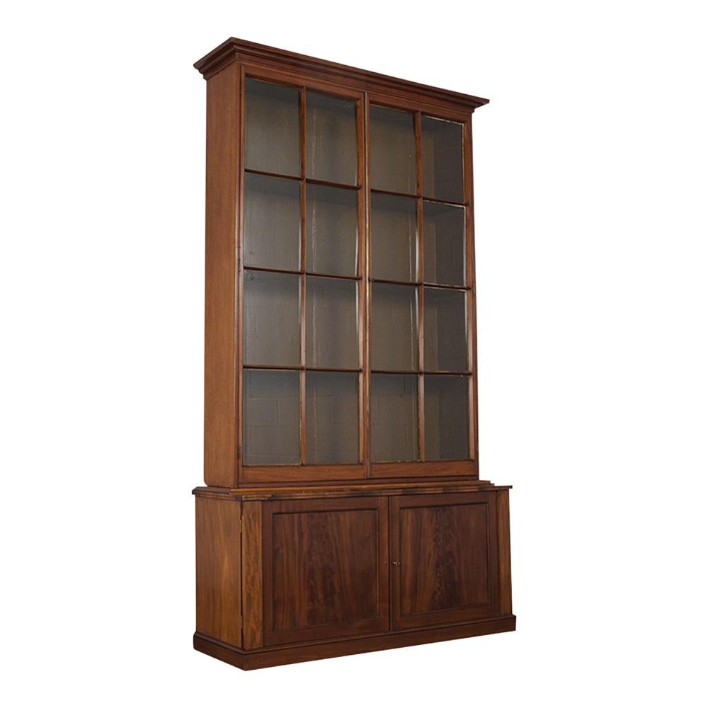 This circa 1840s English mahogany wood Regency style two doors bookcase is a beautiful piece that has been completely restored and features its original dark mahogany finish. It also has two tall glass panels doors divided with very fine molding