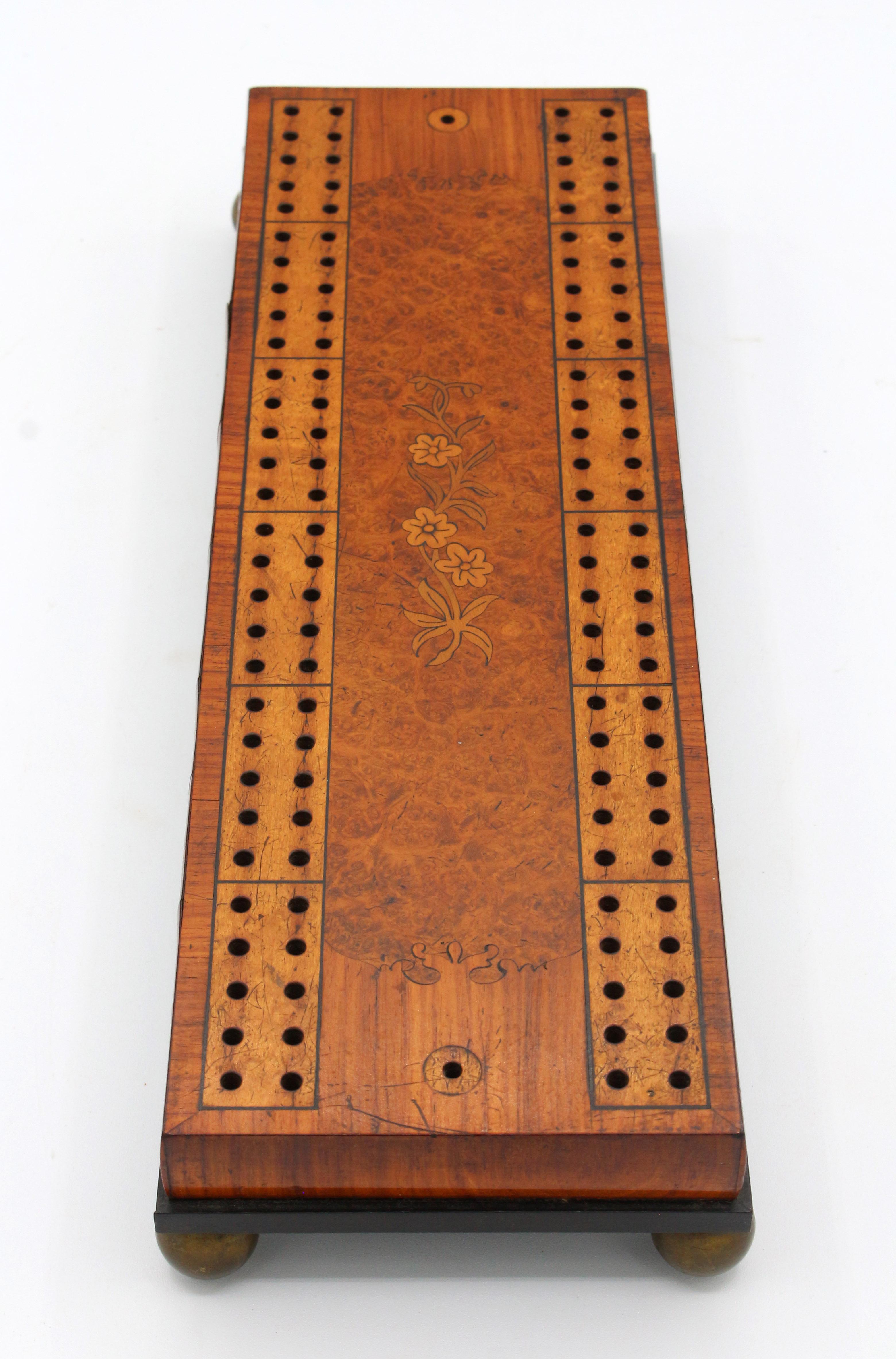 Circa 1860-80 marquetry inlaid cribbage board, English. Burl amboyna wood with walnut, satinwood, boxwood, kingwood & ebony raised on brass ball feet. As fine as they come! Pegs are replacements of turned wood.
12 5/8