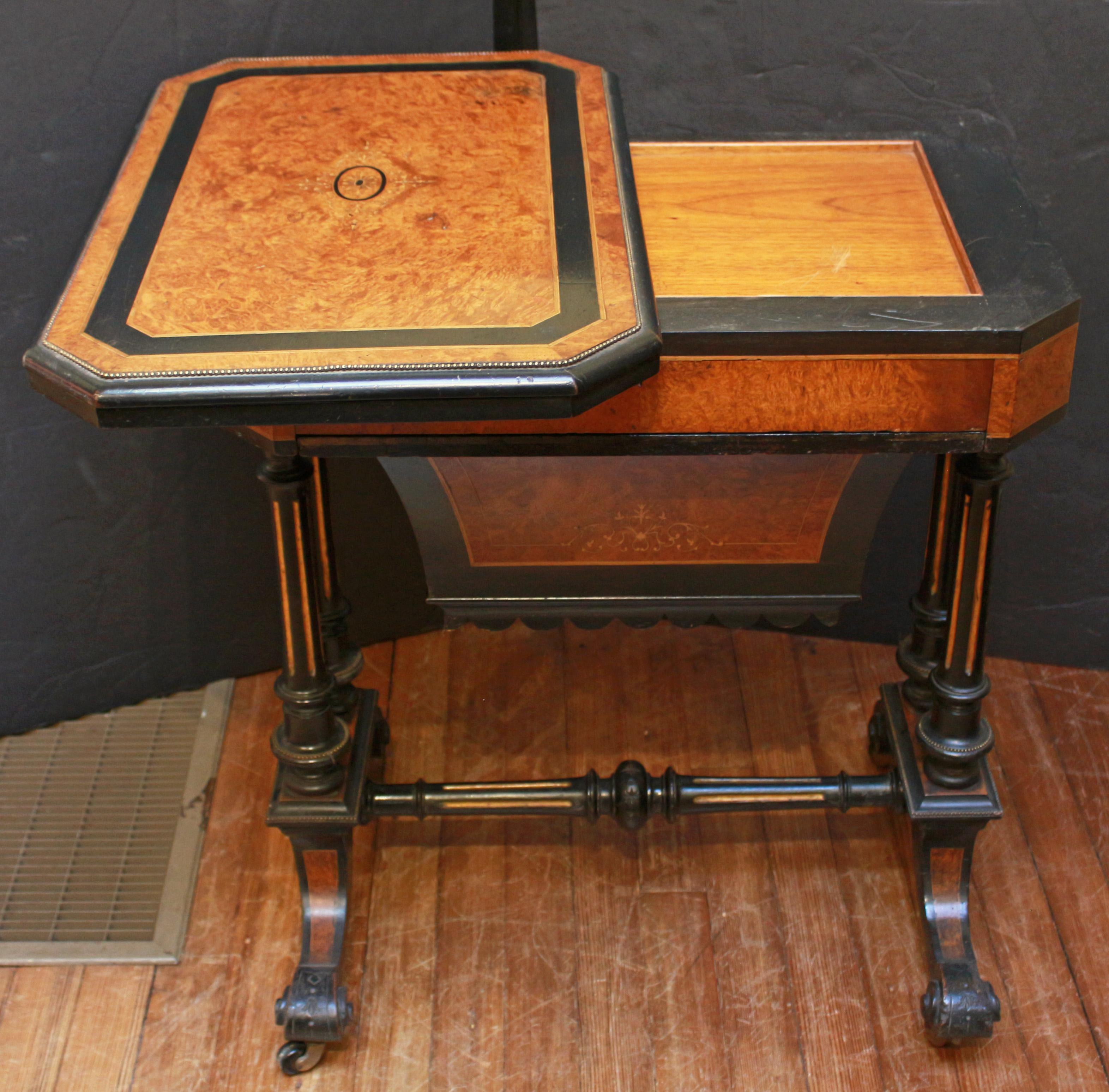 Circa 1860-80 Renaissance Revival Games Table, English. Amboyna avec incrustations d'ébène et de buis. Bordure en laiton. Panier de couture à tiroir. Le plateau pivotant se déplie pour révéler de multiples surfaces de jeu incrustées dans l'ébène -