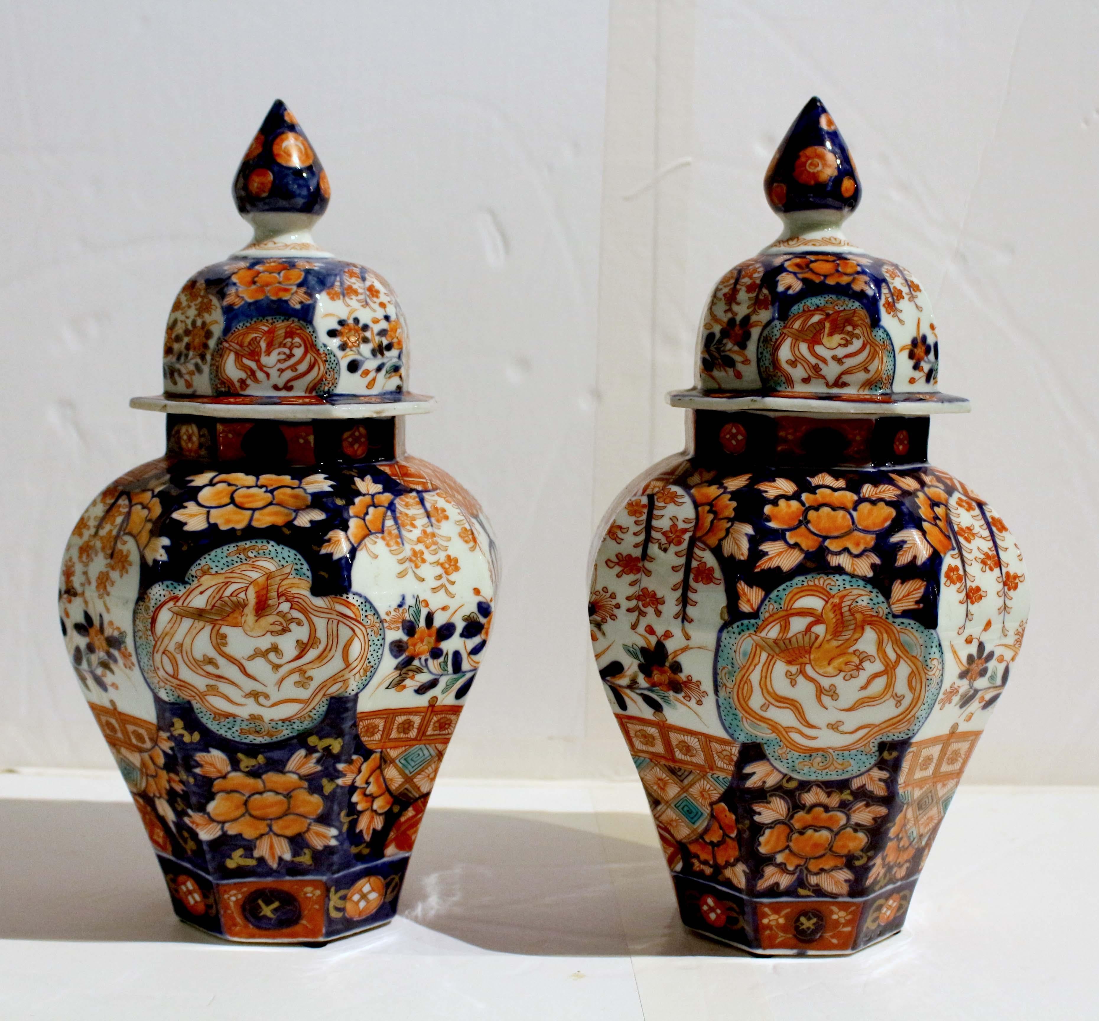 Circa 1860-80 pair of Imari covered jars, Japanese. The lids with finial tops, decorated with phoenix birds & flowers. The jars decorated with large flower vases underneath flowering trees set against geometric designs alternating with cartouches of