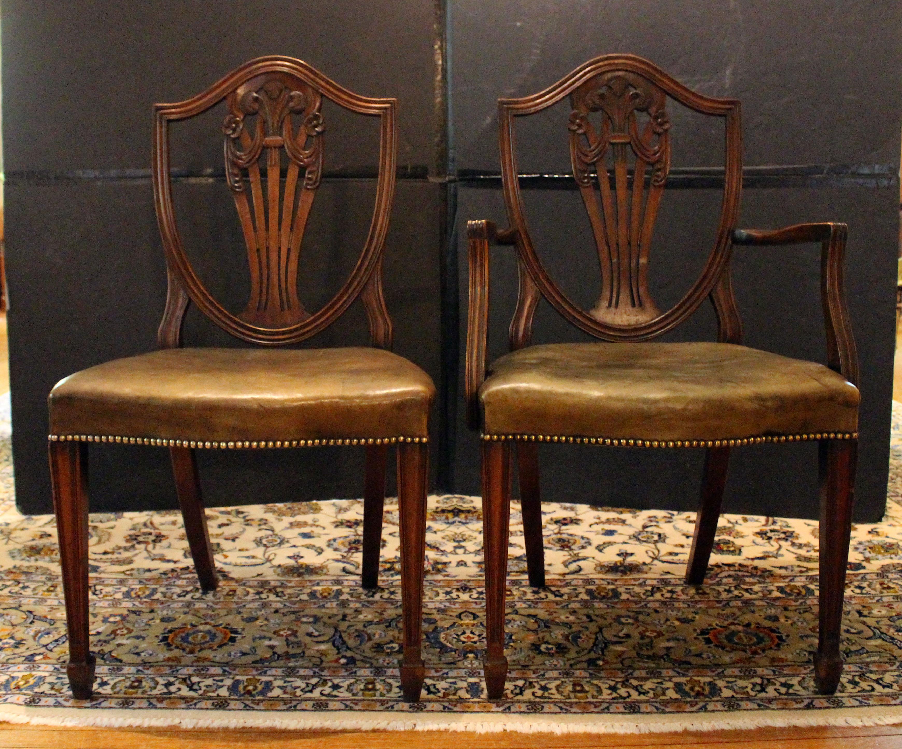 Circa 1860-80 set of 12 Georgian style dining chairs, English. 10 sides & 2 arms. Georgian Revival period of excellent quality. Shield backs with Prince of Wales plume, rosette & swag carved backsplats. The chairs have serpentine seats & fine old