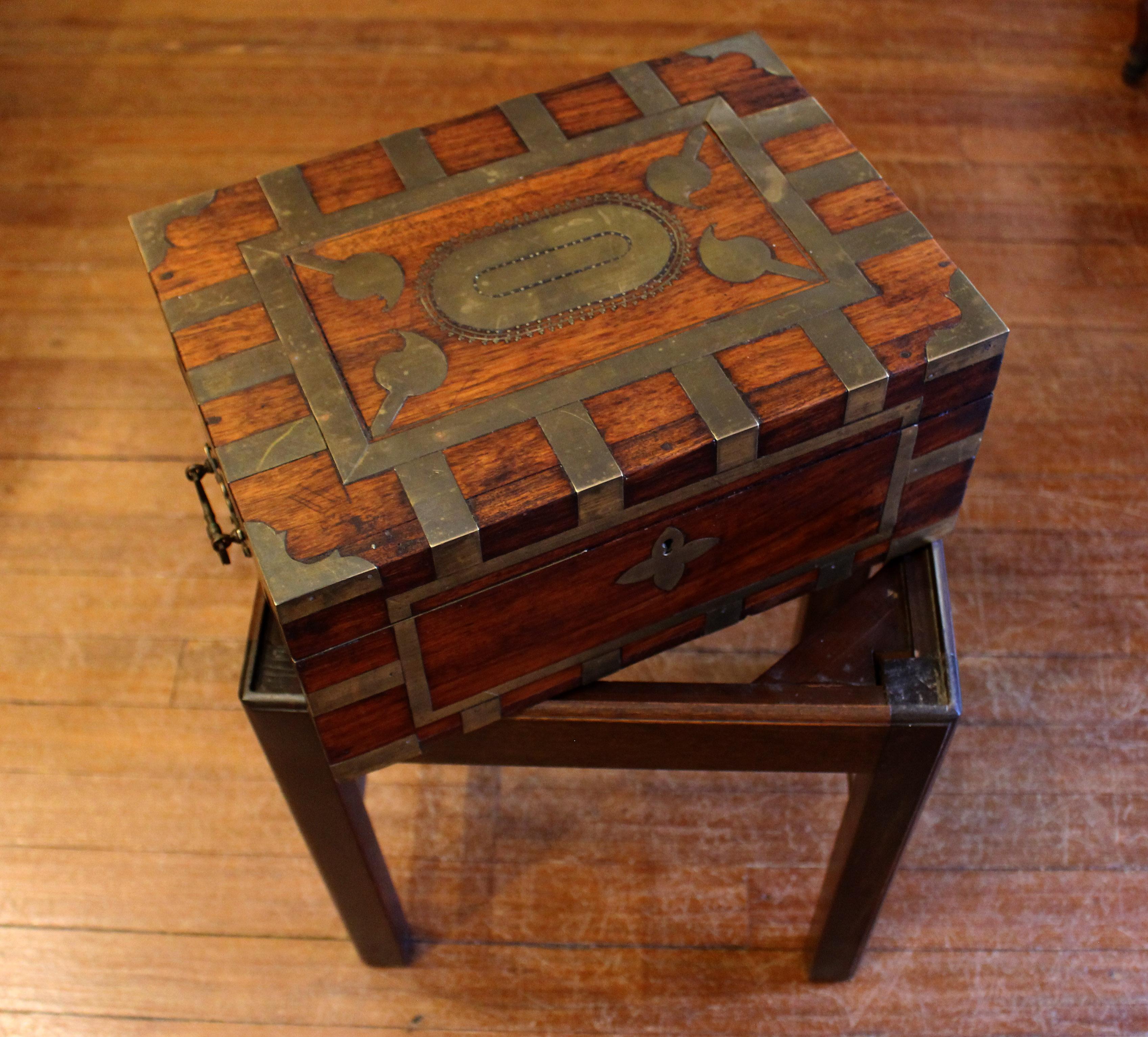 Circa 1870 Anglo-Indian travel box now on custom made side table stand. Teak wood, extravagantly brass bound. Compartmented, lidded lift-out interior tray. Carrying handles. Raj period. Measures: Overall 14 1/8