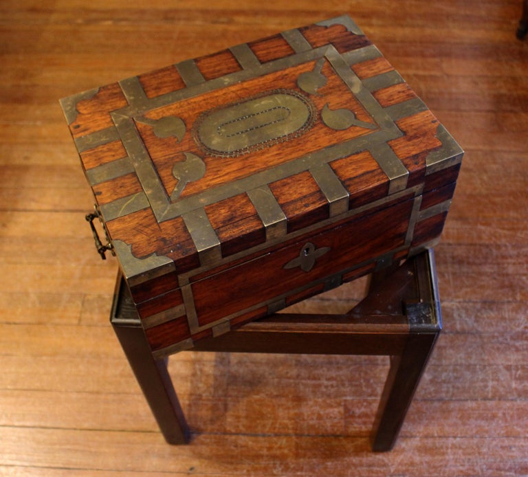Circa 1870 Anglo-Indian travel box now on custom made side table stand. Teak wood, extravagantly brass bound. Compartmented, lidded lift-out interior tray. Carrying handles. Raj period. Measures: Overall 14 1/8