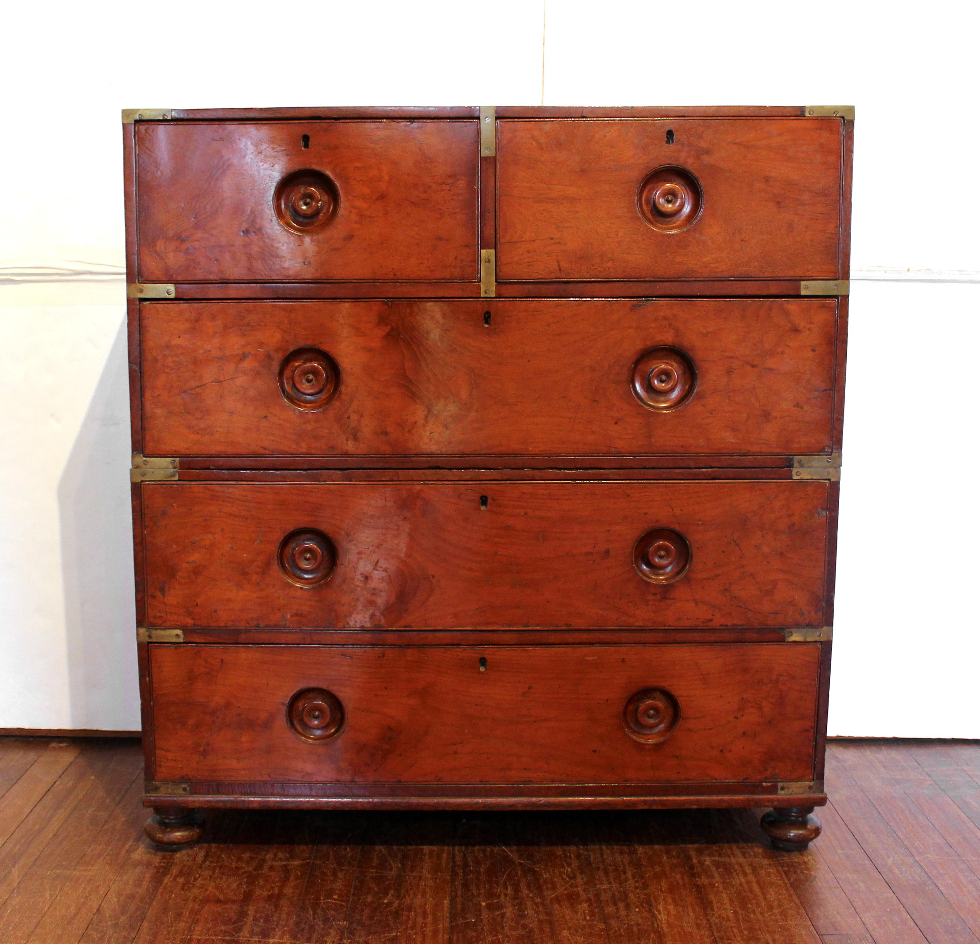 Circa 1860 campaign chest of drawers, English. Teak. Two-section design with iron side carrying handles for transport. Bun feet. Recessed treen pulls. Brass corner brackets & strapping mounts. Lacks escutcheons. Various finish imperfections, mars &