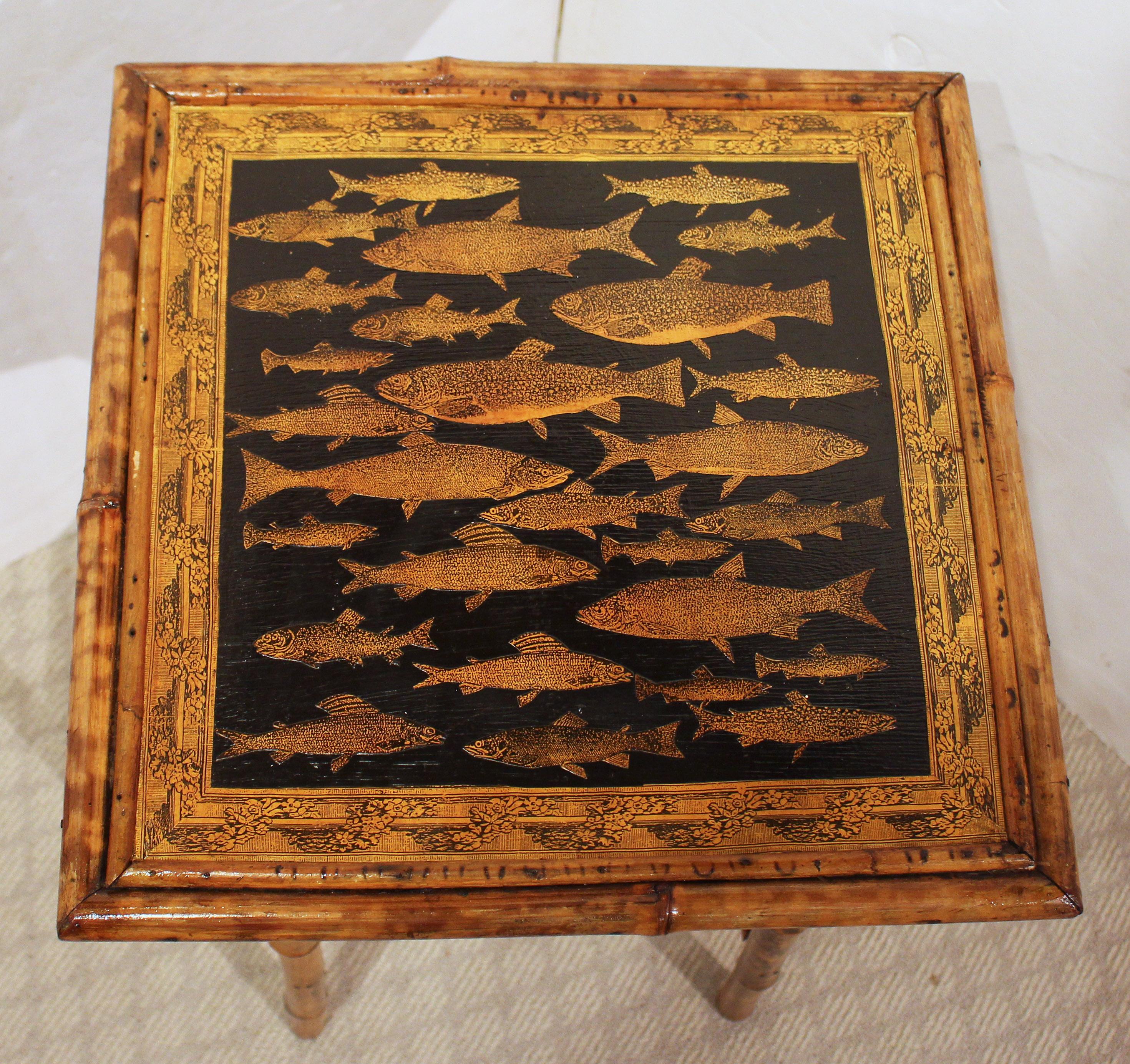 Mesa cuadrada de bambú, inglesa, circa 1870. La superficie original ahora decorada artesanalmente con peces. El estante arquitectónico inferior ofrece un atractivo lugar para revistas o libros grandes. Puntales diagonales en la parte superior. Bambú