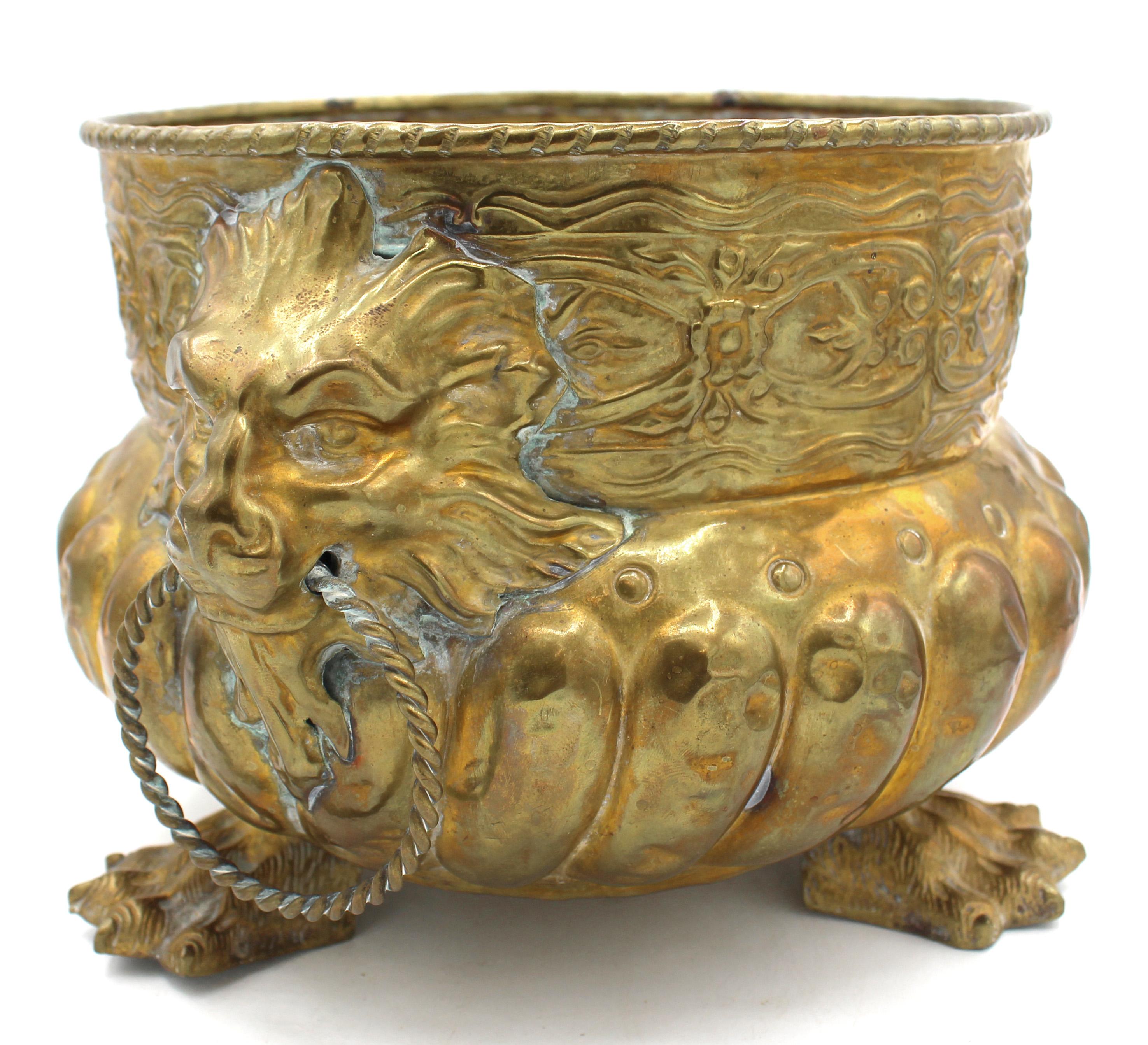 Circa 1880 circular brass jardiniere, English. Repousse work, raised on bold cast paw feet. Great lion mask handles with twisted rings. Denting of gadroon body. 10