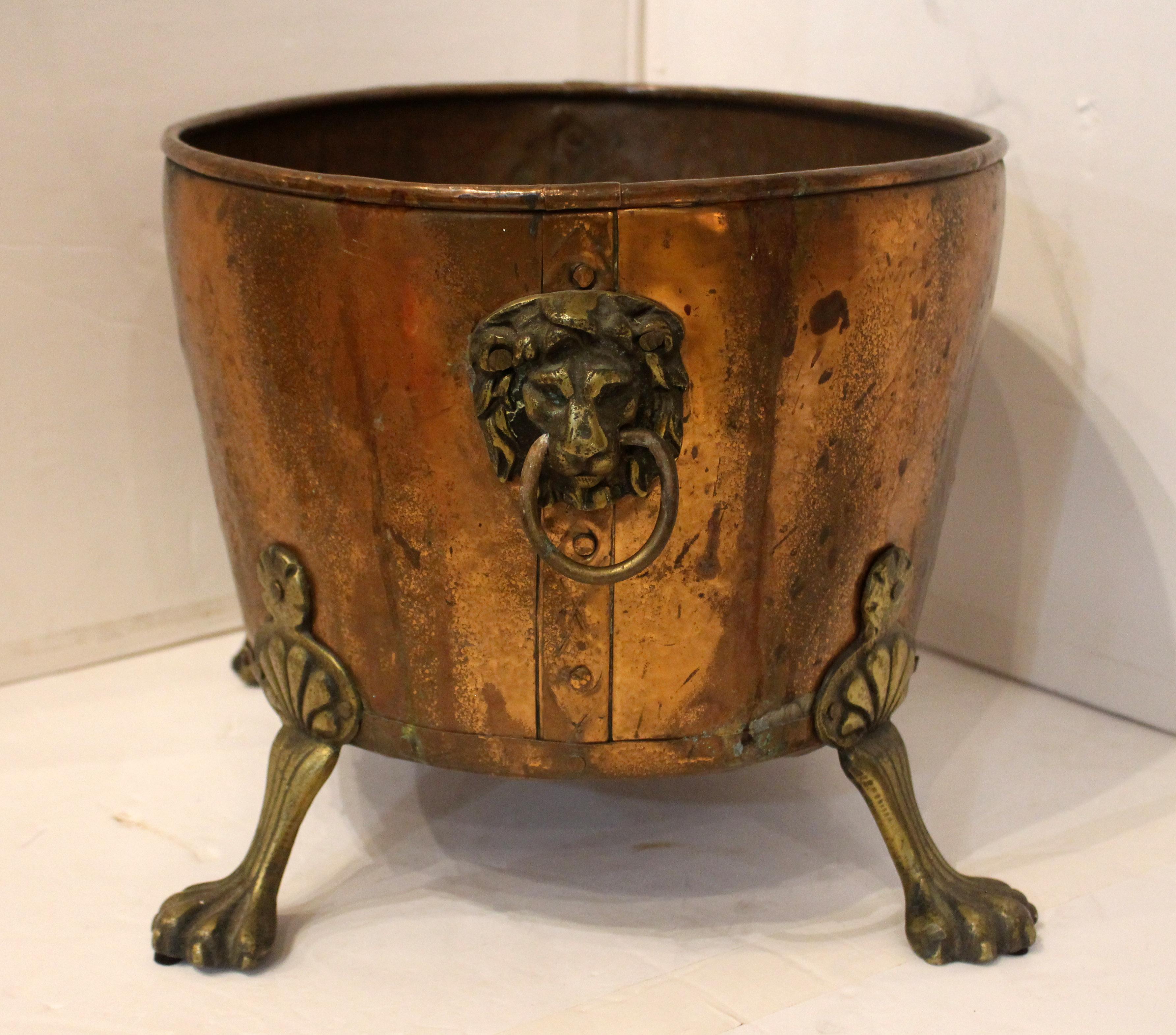 Circa 1880 copper & brass jardiniere or log bin, English. Copper strap & rivets seam construction accents the design. Bold brass lion mask ring turned handles and raised on shaped lion's paw feet. Also ideal as a beer/wine cooler for entertaining.