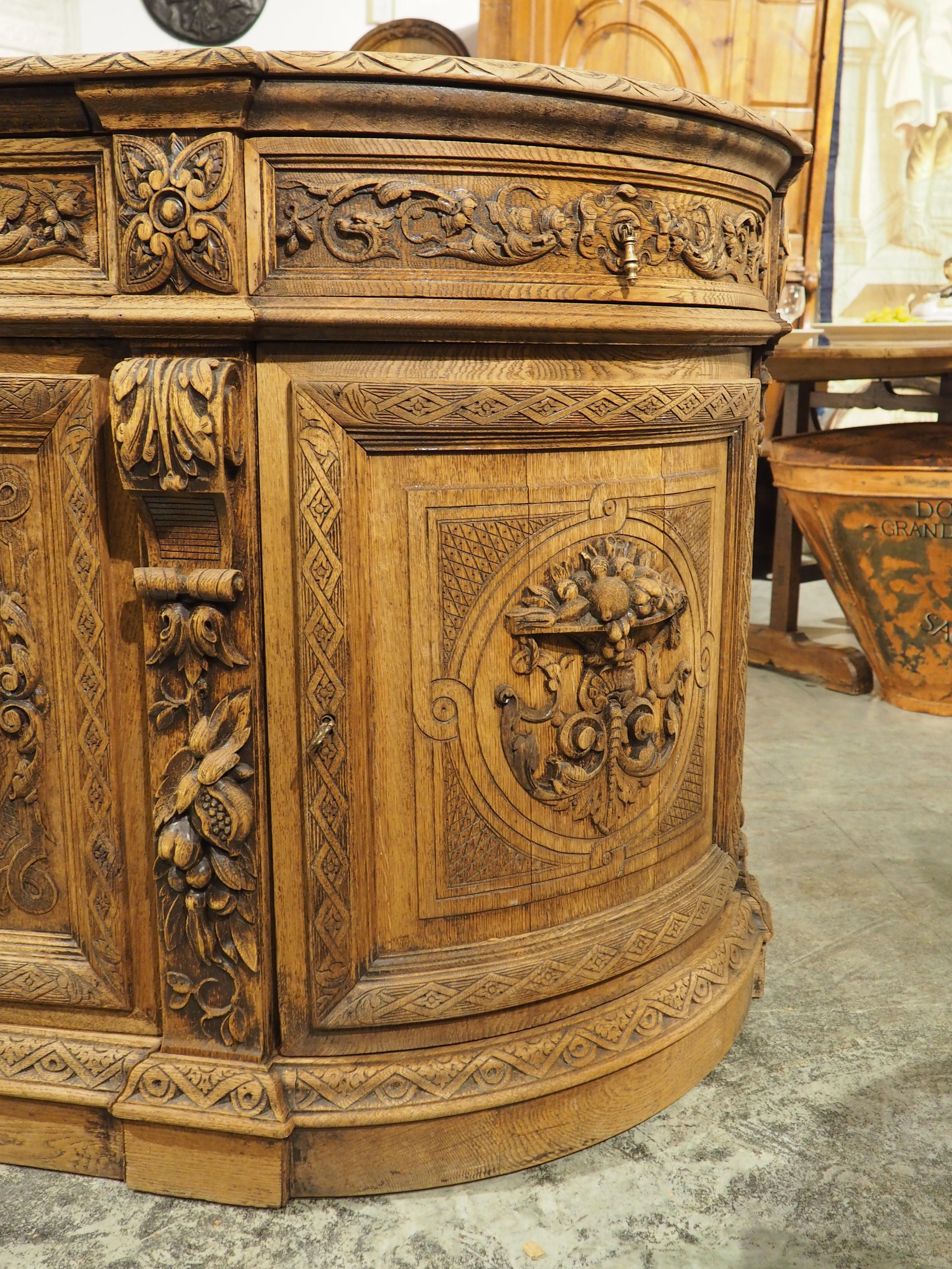 From France, circa 1880, this exceptional buffet features curved ends, giving the cabinet an overall demilune shape. Carved by hand by an immensely talented woodworker, the motifs on the two center doors depict a fowl trophy (left door) and a fish