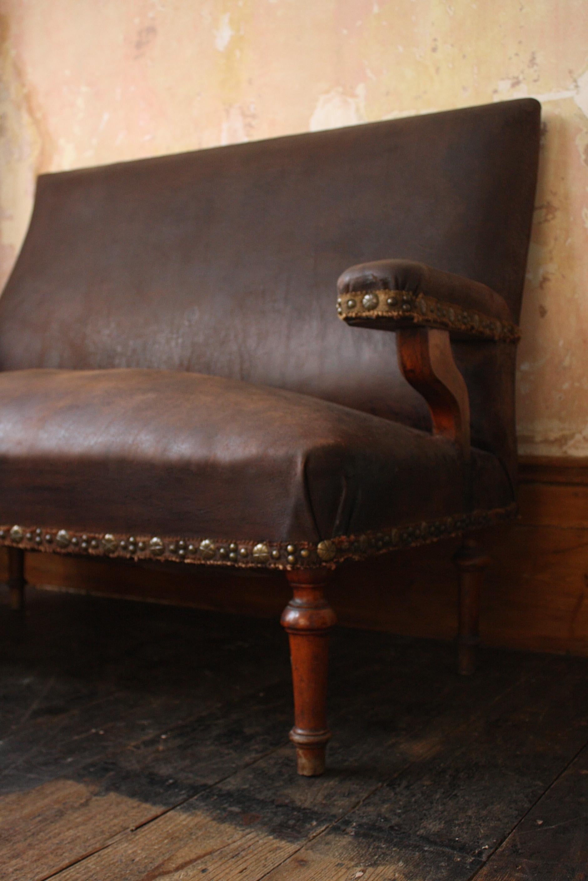 French shapely hall settle/bench, circa 1880 in age with its original dark brown leather upholstery and decorative brass stud work fringing.

On turned oak legs, one has had an elderly repair and shows signs of some minor old long vacated word